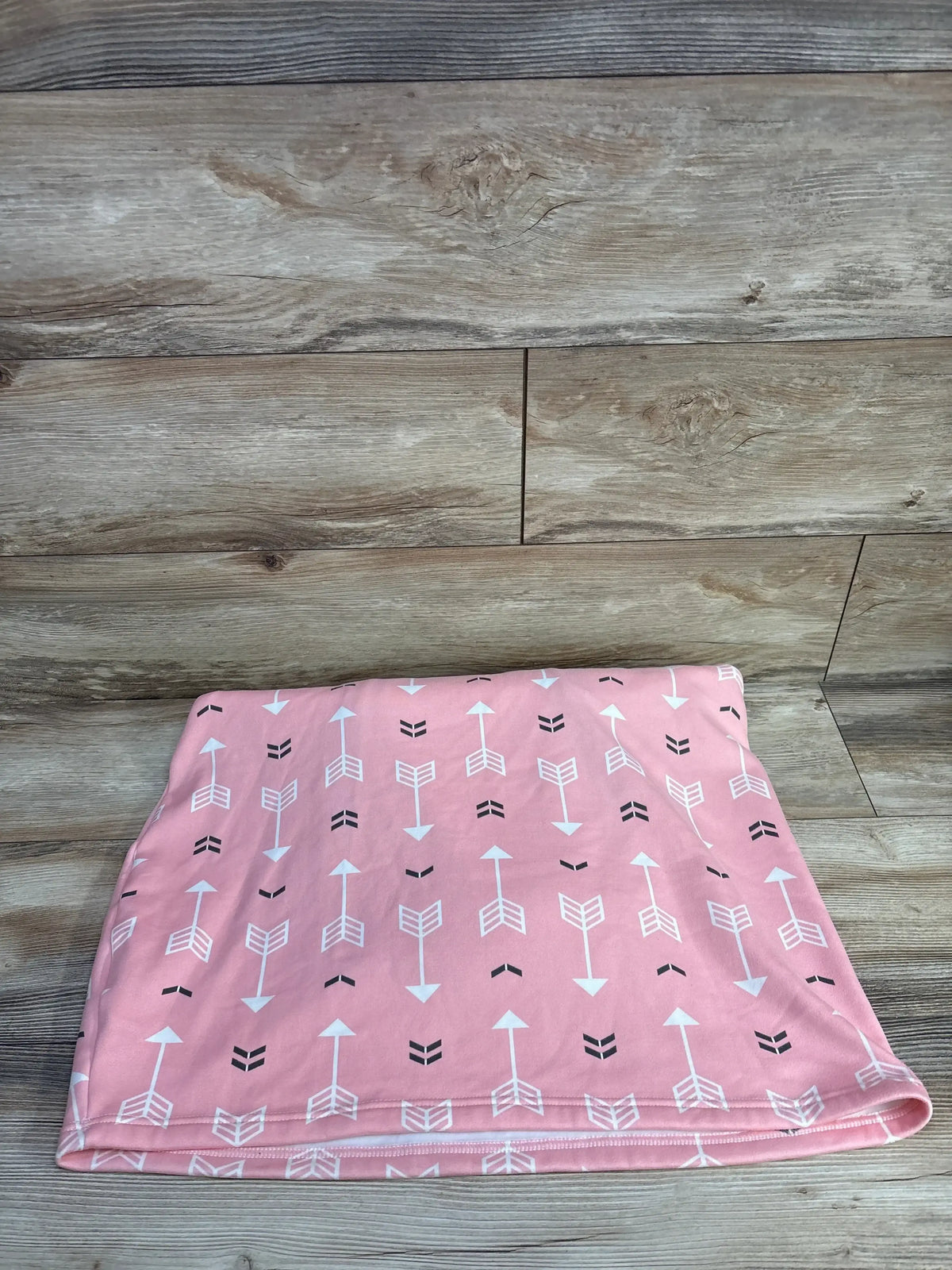 Folded view of Acrabros car seat cover showcasing pink fabric with white and black arrow print on wood plank background