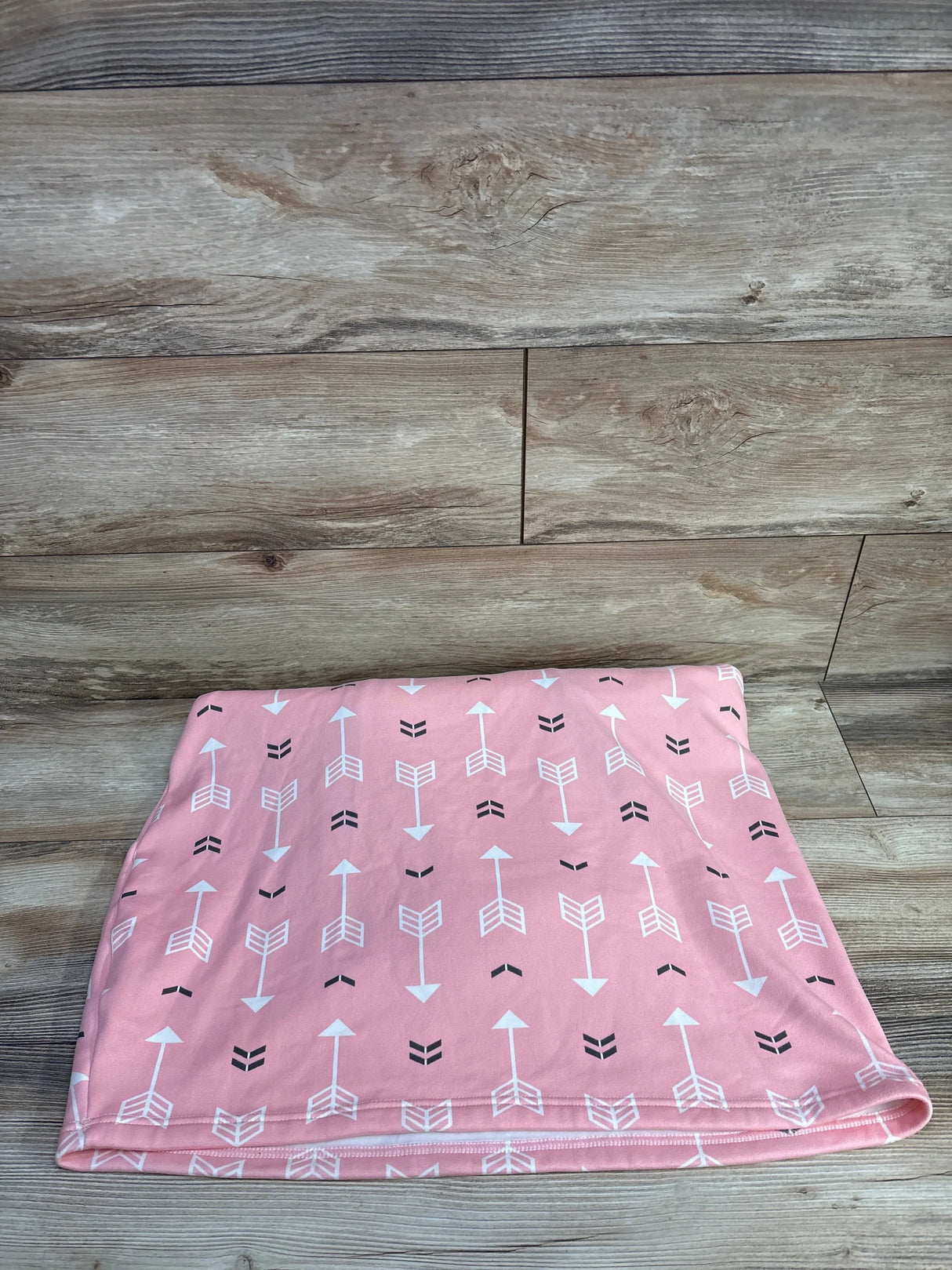 Pink baby blanket with white and black arrow pattern on wood background