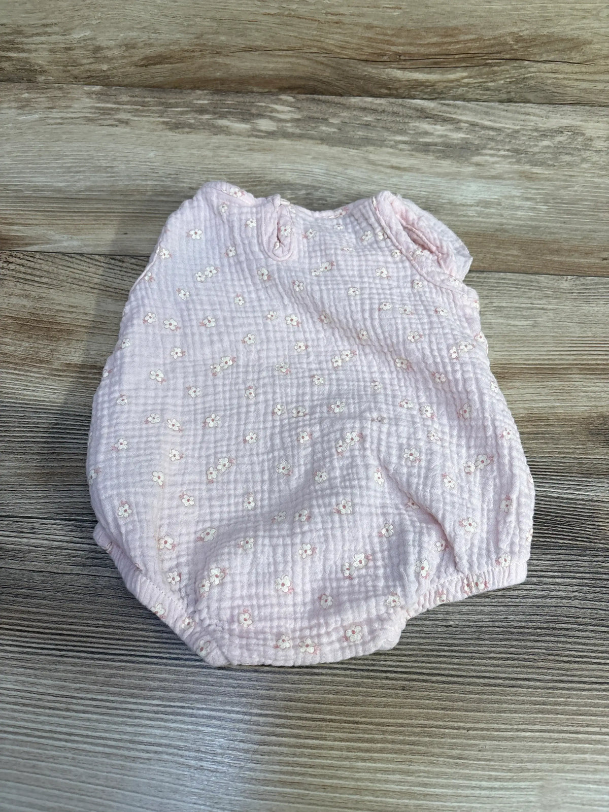 Flat lay of Chick Pea pink bubble romper with textured muslin and small white floral print on wood background