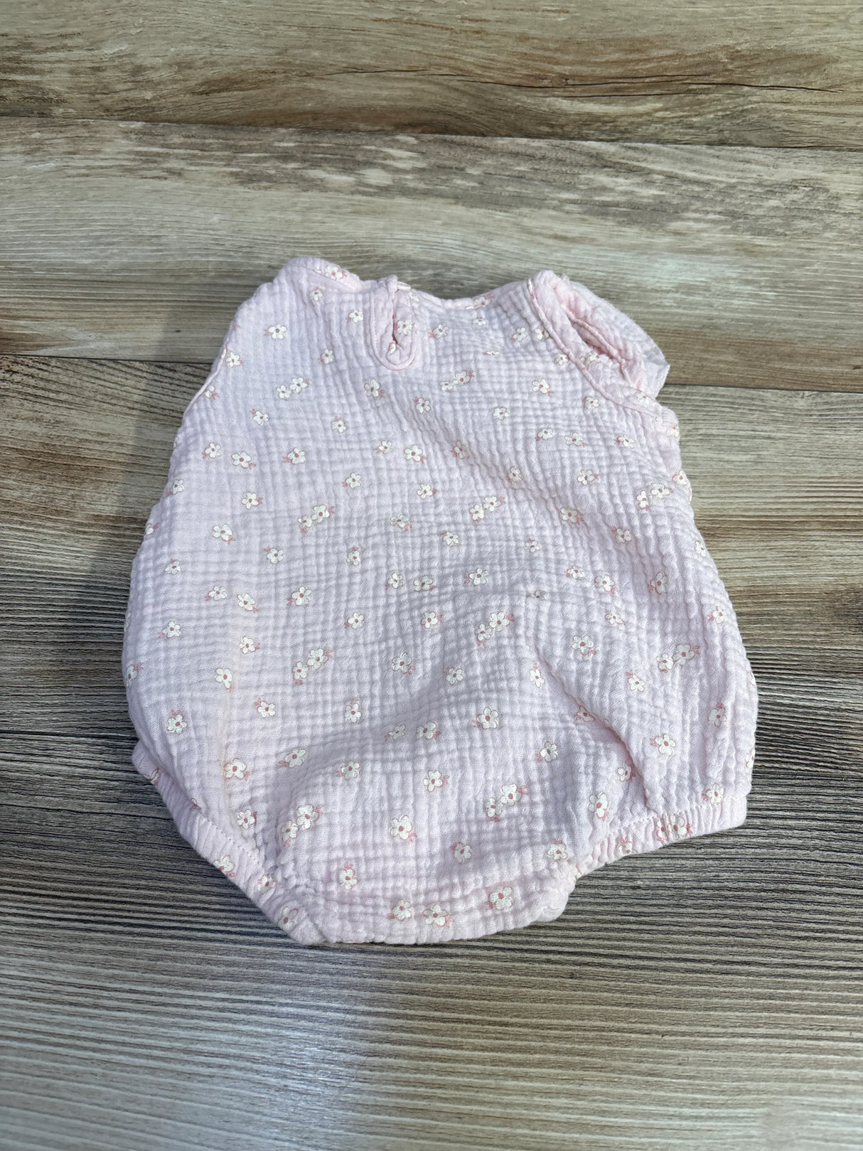 Flat lay of Chick Pea pink bubble romper with textured muslin and small white floral print on wood background