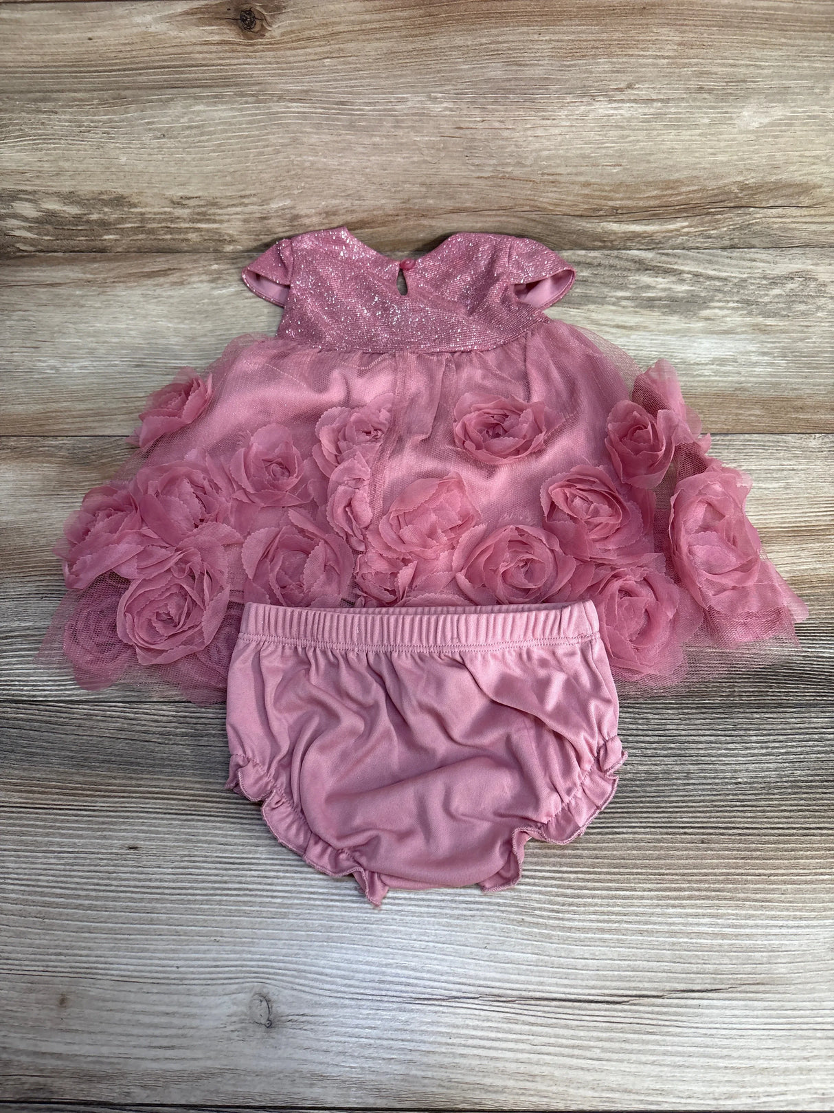 Pink baby dress with rosette flowers and matching bloomers on wood background
