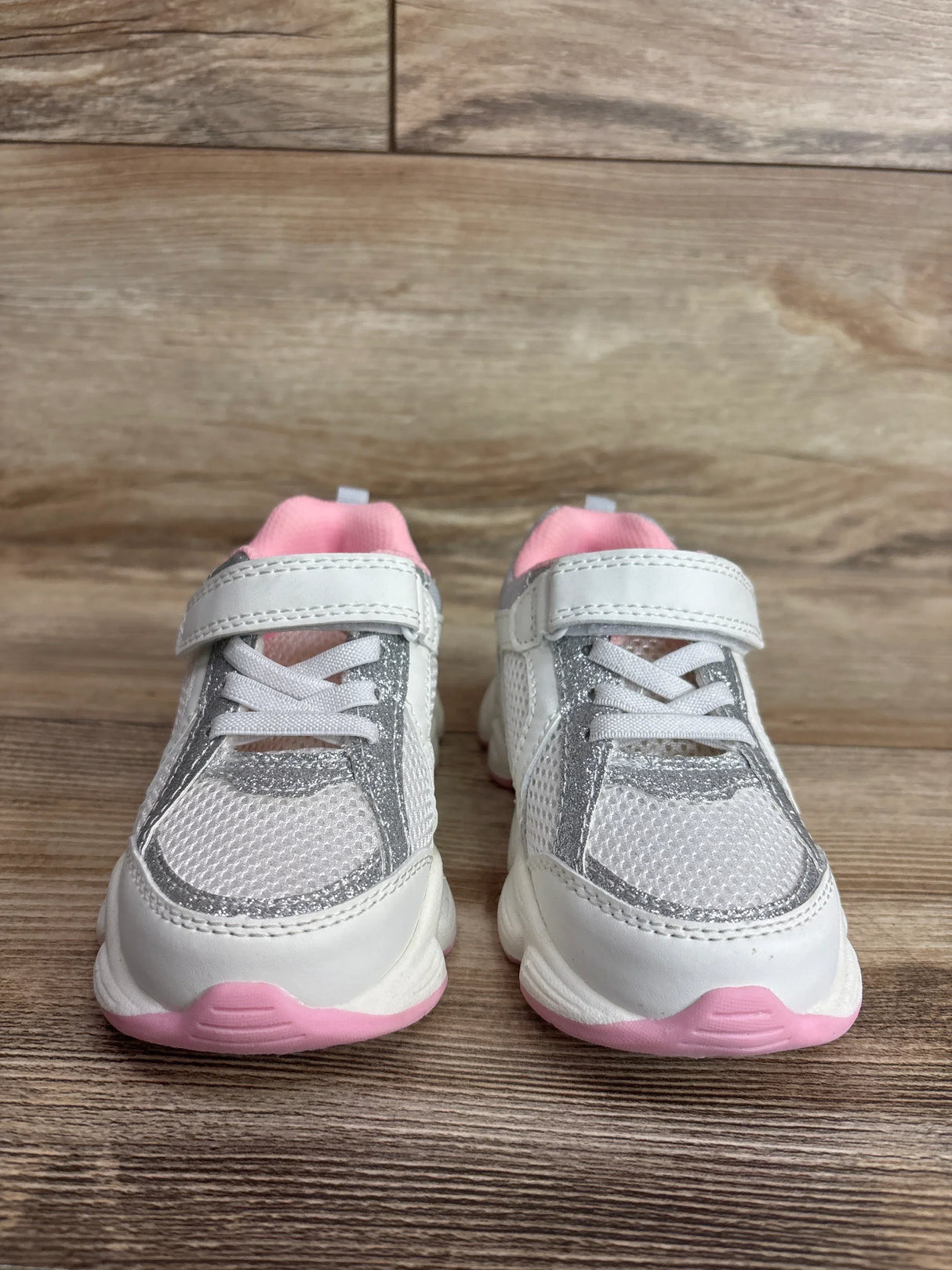 Front view of Carter's toddler white sneakers with silver glitter trim, pink lining and pink soles on wood floor
