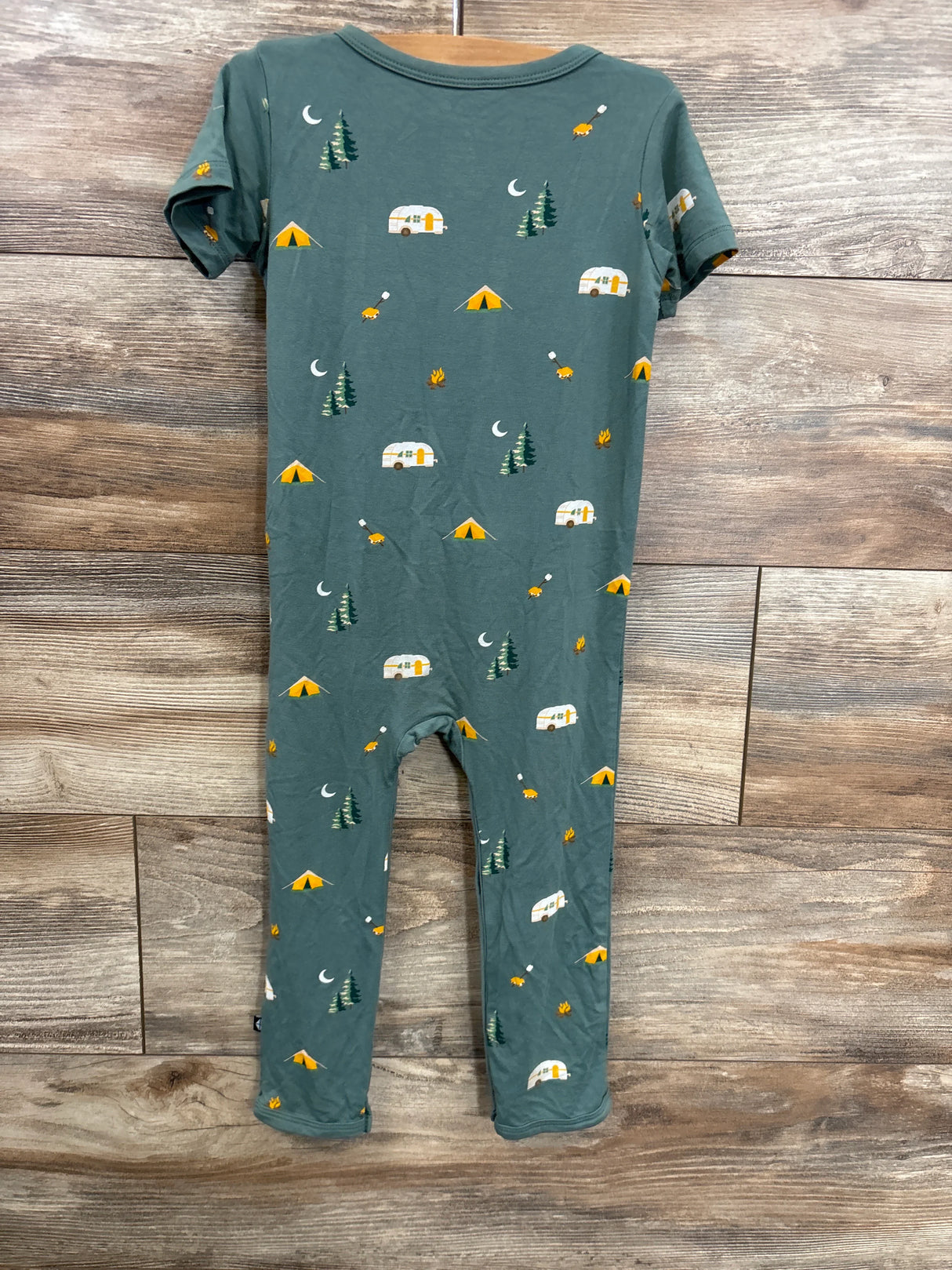 Green kids romper with camping-themed print, tents, trees, and camper vans, on wood background