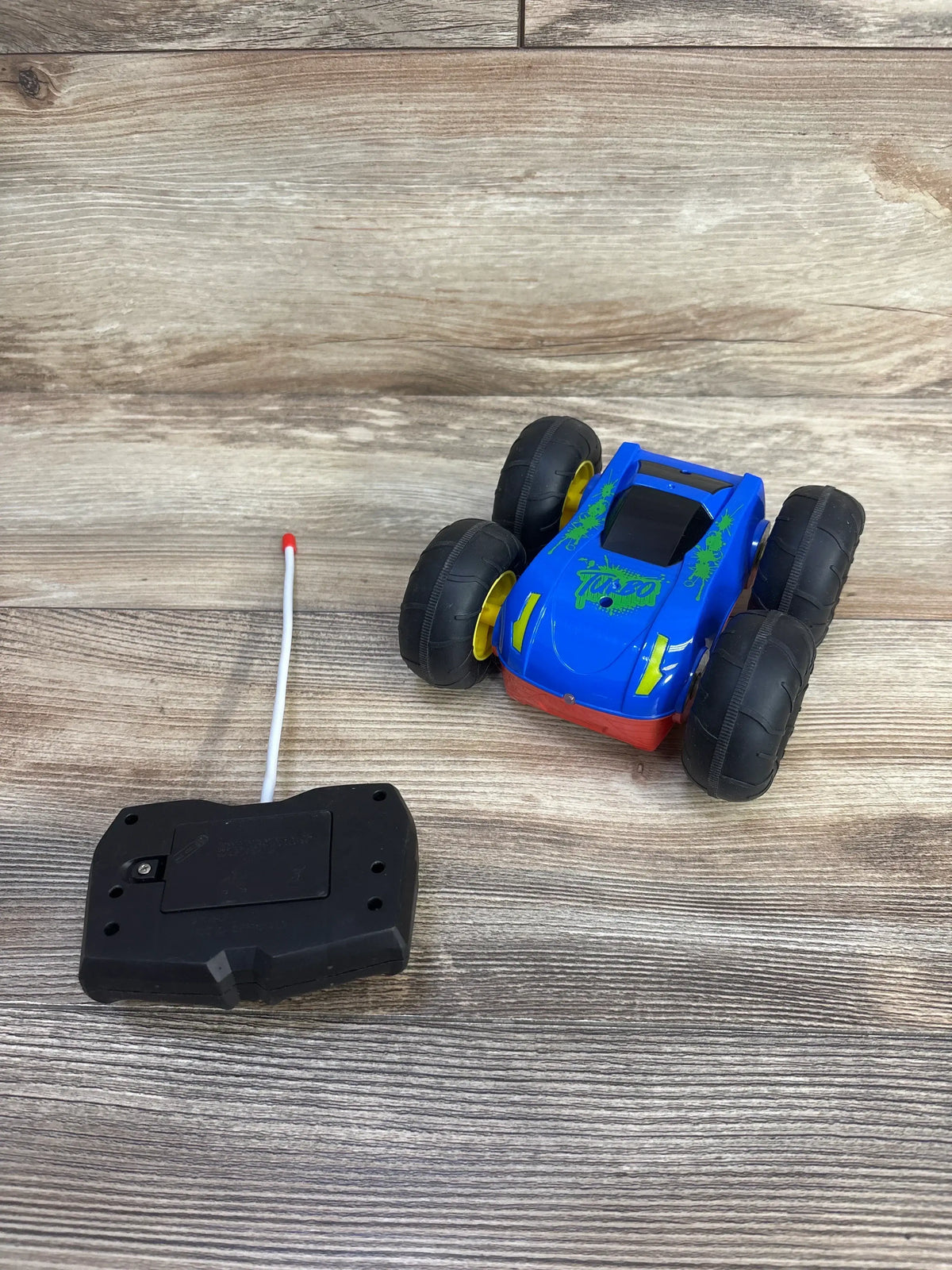 Front three-quarter view of Turbo Wheel Radio Control Stunt Racer Car with remote control and large wheels on a wood-grain background