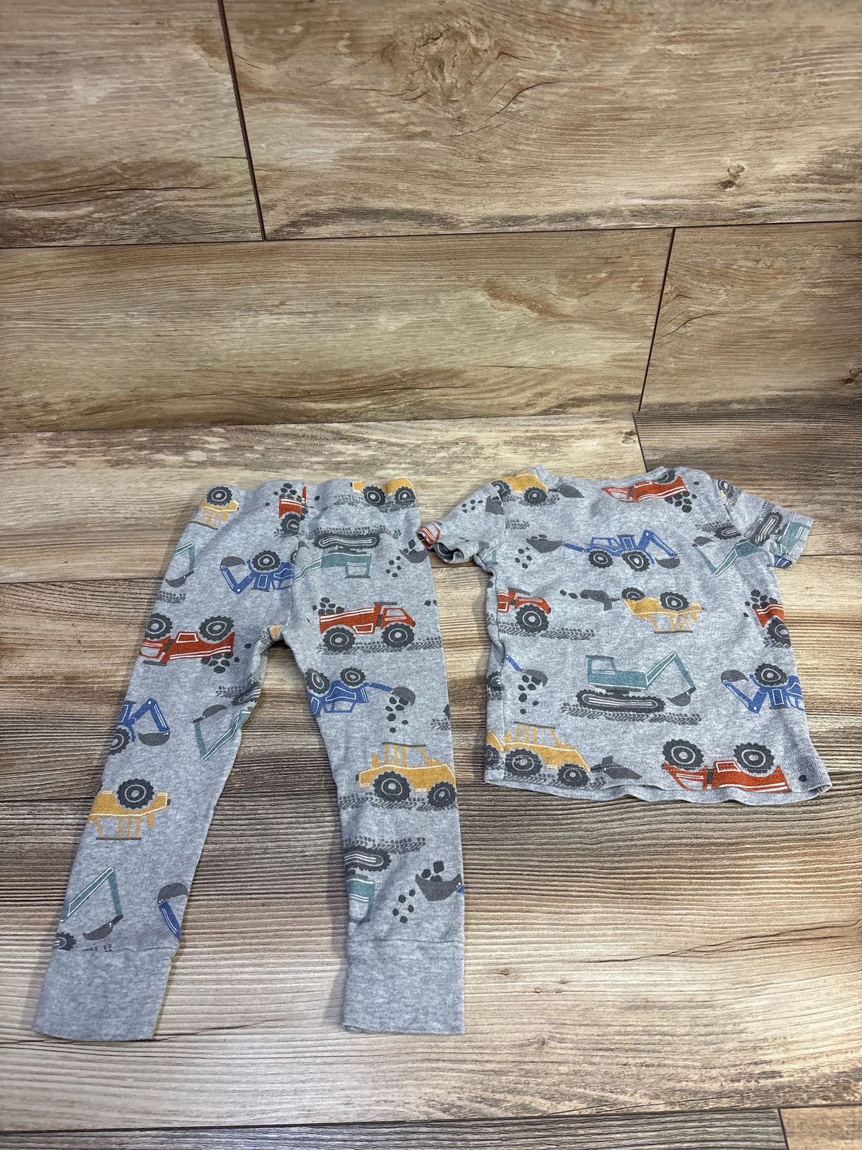 Flat lay of Kids Headquarters 2-piece grey construction vehicle pajama set with colorful truck print on wood background