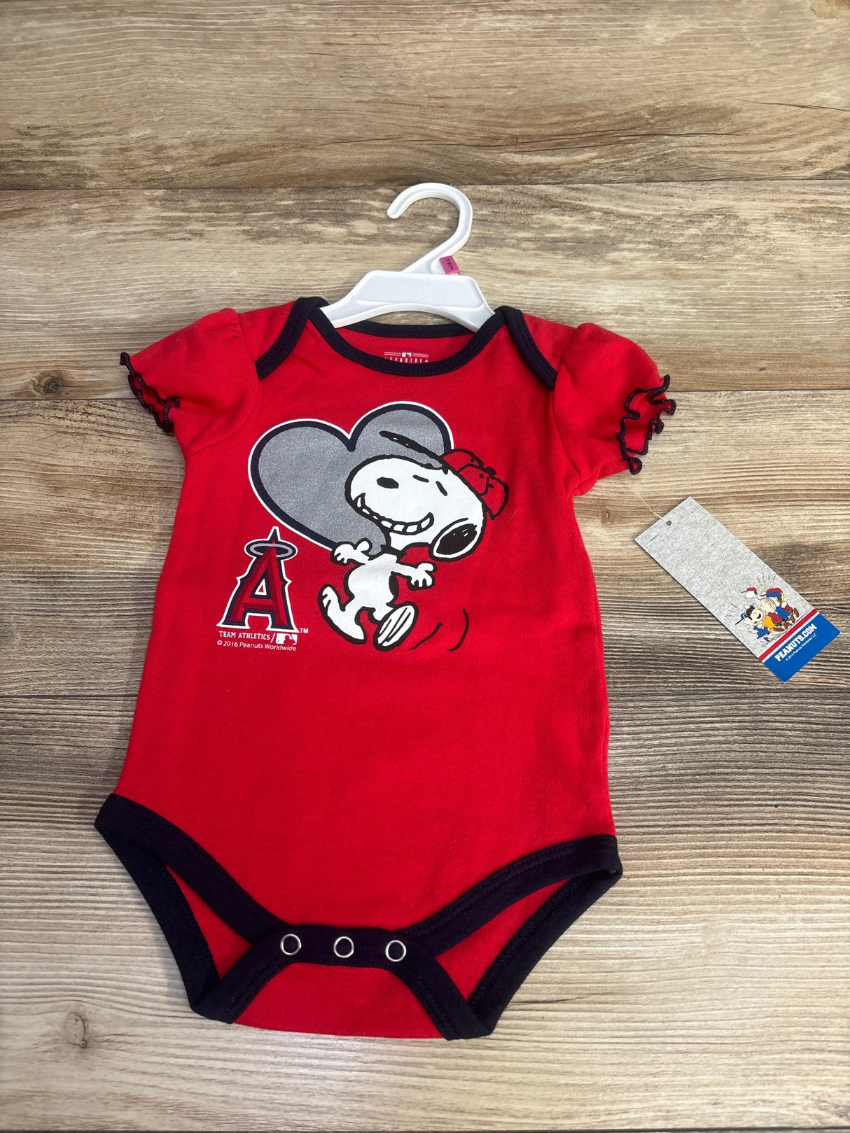 Red Snoopy Angels baby onesie with black trim on wooden background, Peanuts tag visible