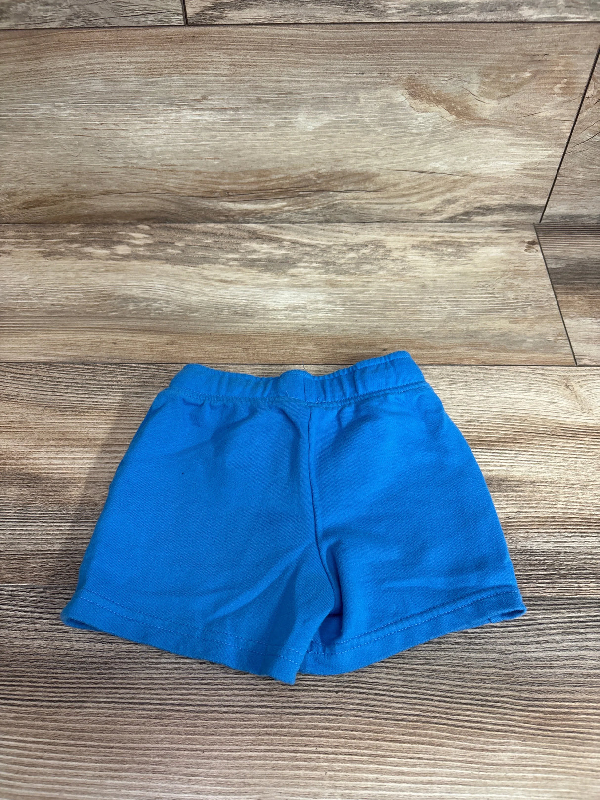 Flat lay of blue Cat & Jack toddler drawstring shorts showing elastic waistband and stitched hem on wood floor background