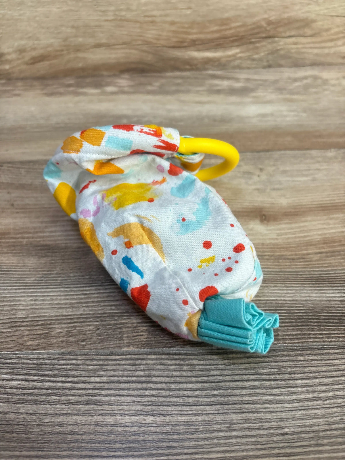 Angled view of Lovevery Organic Cotton Sensory Pouch showcasing colorful fabric, yellow ring, and turquoise ruffle