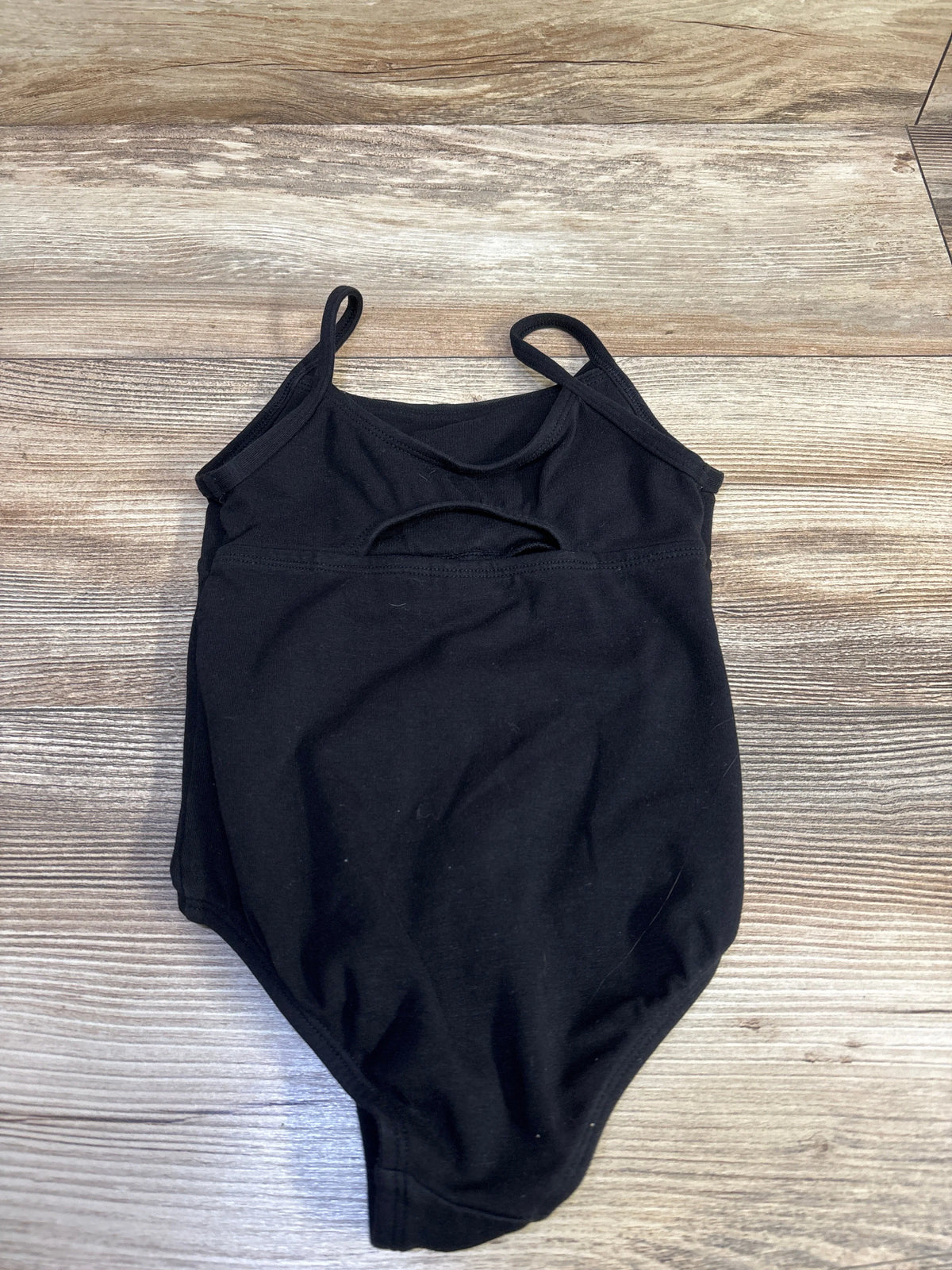 Front view of More Than Magic black leotard, size 4T, showcasing thin straps and an oval chest cutout on a wood-grain surface