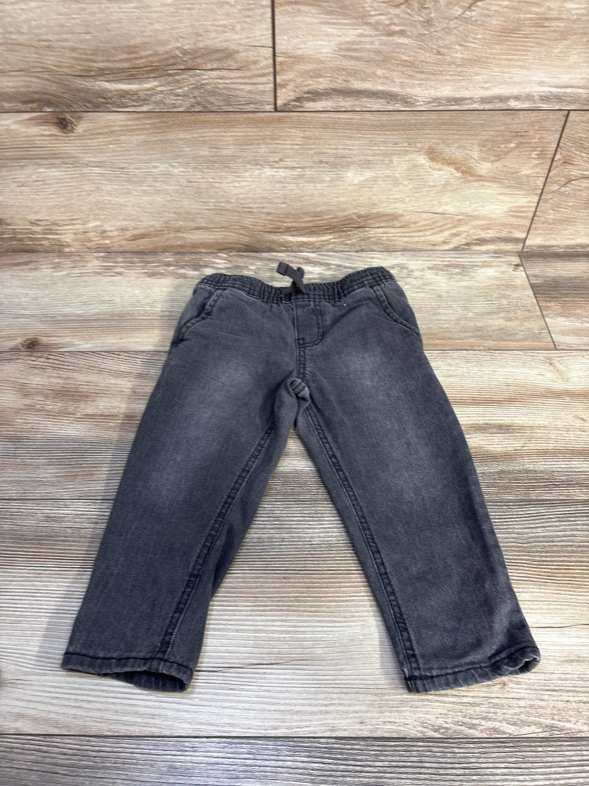 Front view of OshKosh grey drawstring jeans in size 24m showcasing the adjustable waist on a wood-look floor
