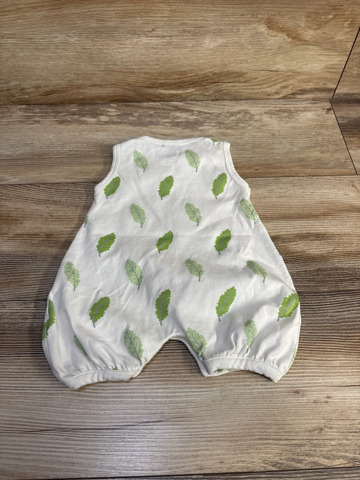 Laid flat view of Kissy Love leaf print romper in white size 3 to 6 months showcasing short sleeves and legs on wood floor