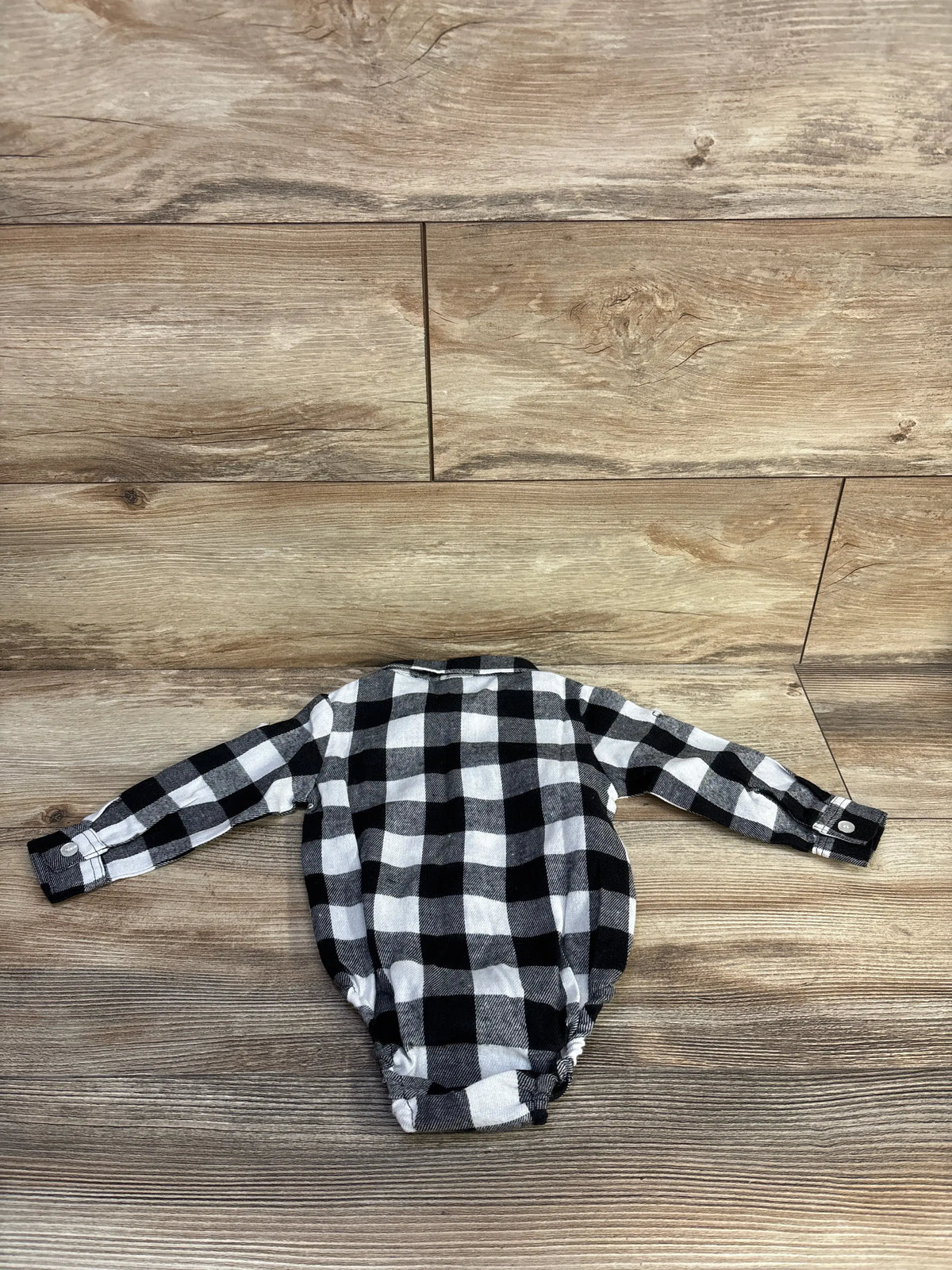 Top view of black plaid flannel bodysuit in size 12 months showcasing long sleeves on a wood-look background