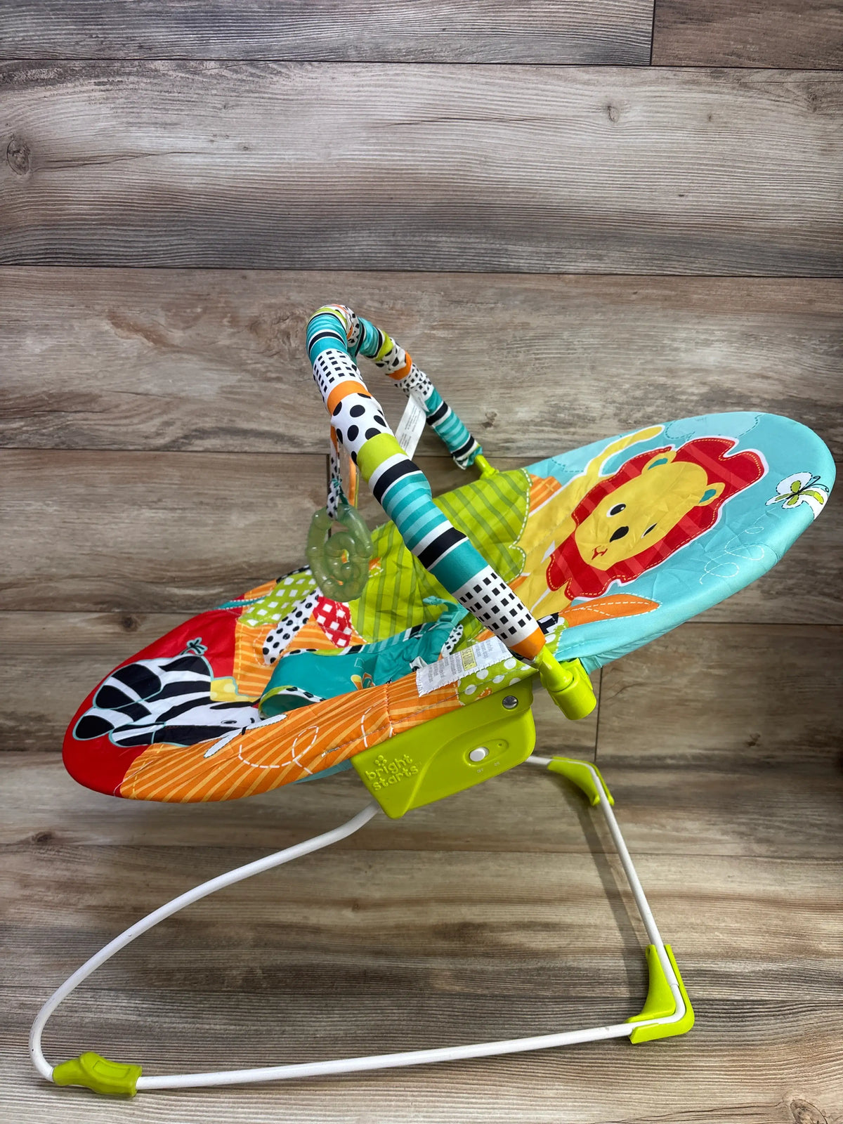 Side view of Bright Starts Roaming Safari Vibrating Baby Bouncer showcasing colorful safari print and toy bar with wood plank background