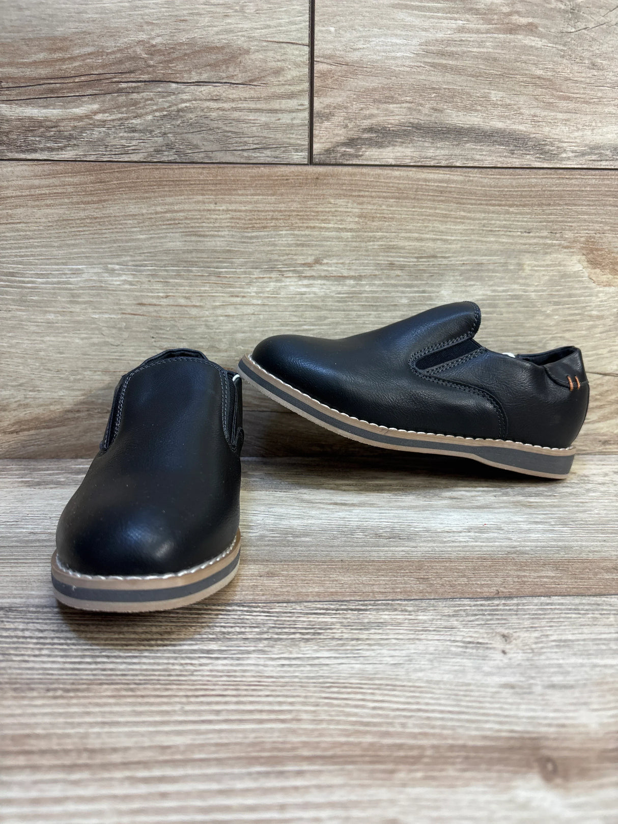 Black slip-on kids shoes with tan soles on wood background, children's footwear resale