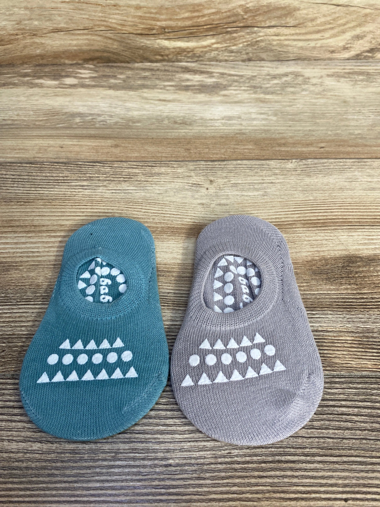 Top-down view of two non-slip baby socks, blue and grey, showing white triangle-and-dot grip pattern on light wood background