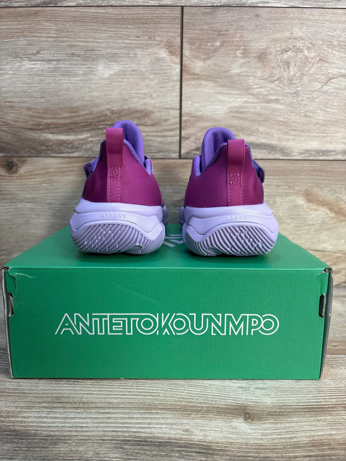 Pink and purple kids athletic shoes on green Antetokounmpo shoe box, wood background