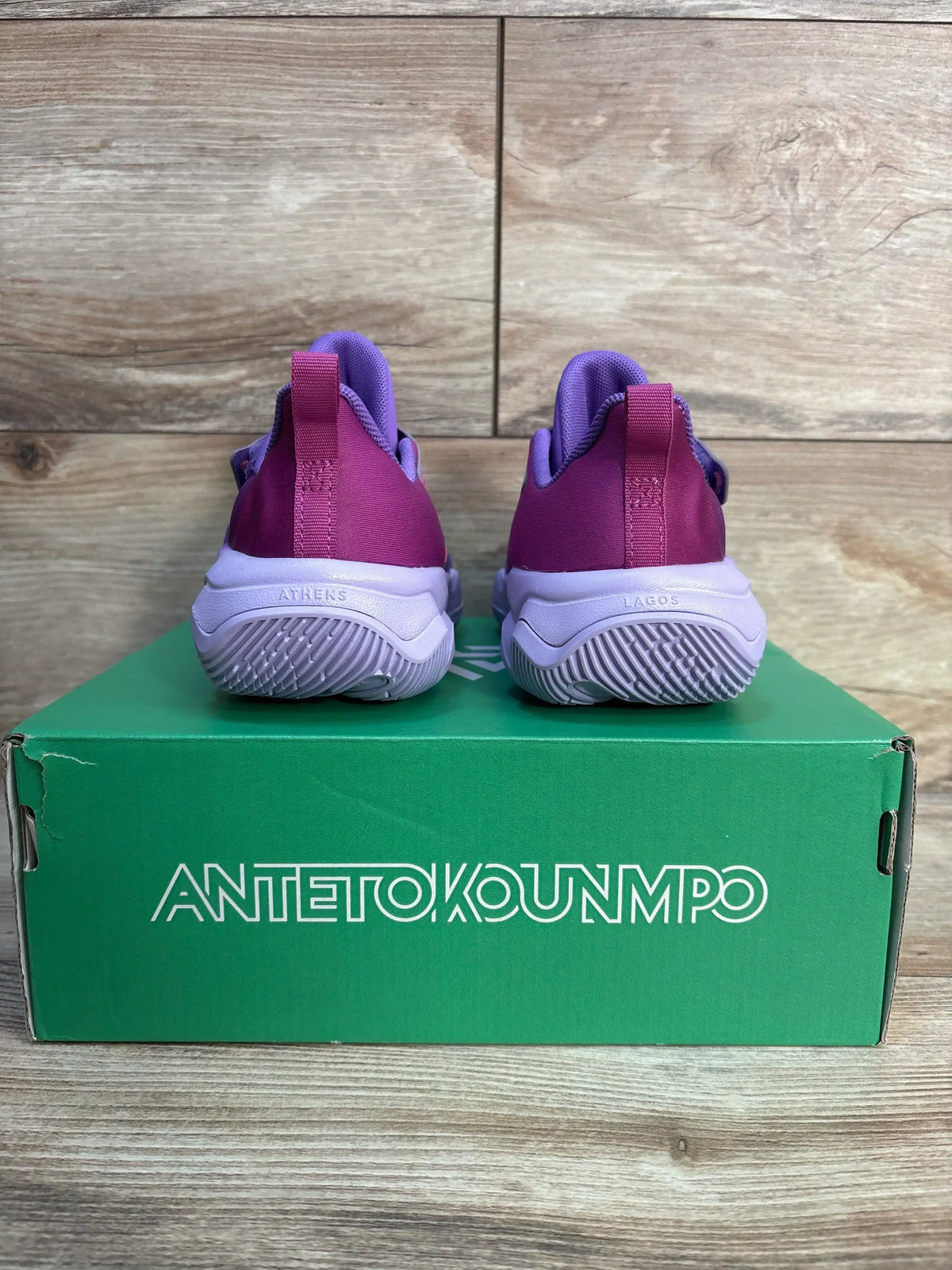 Pink and purple kids athletic shoes on green Antetokounmpo shoe box, wood background
