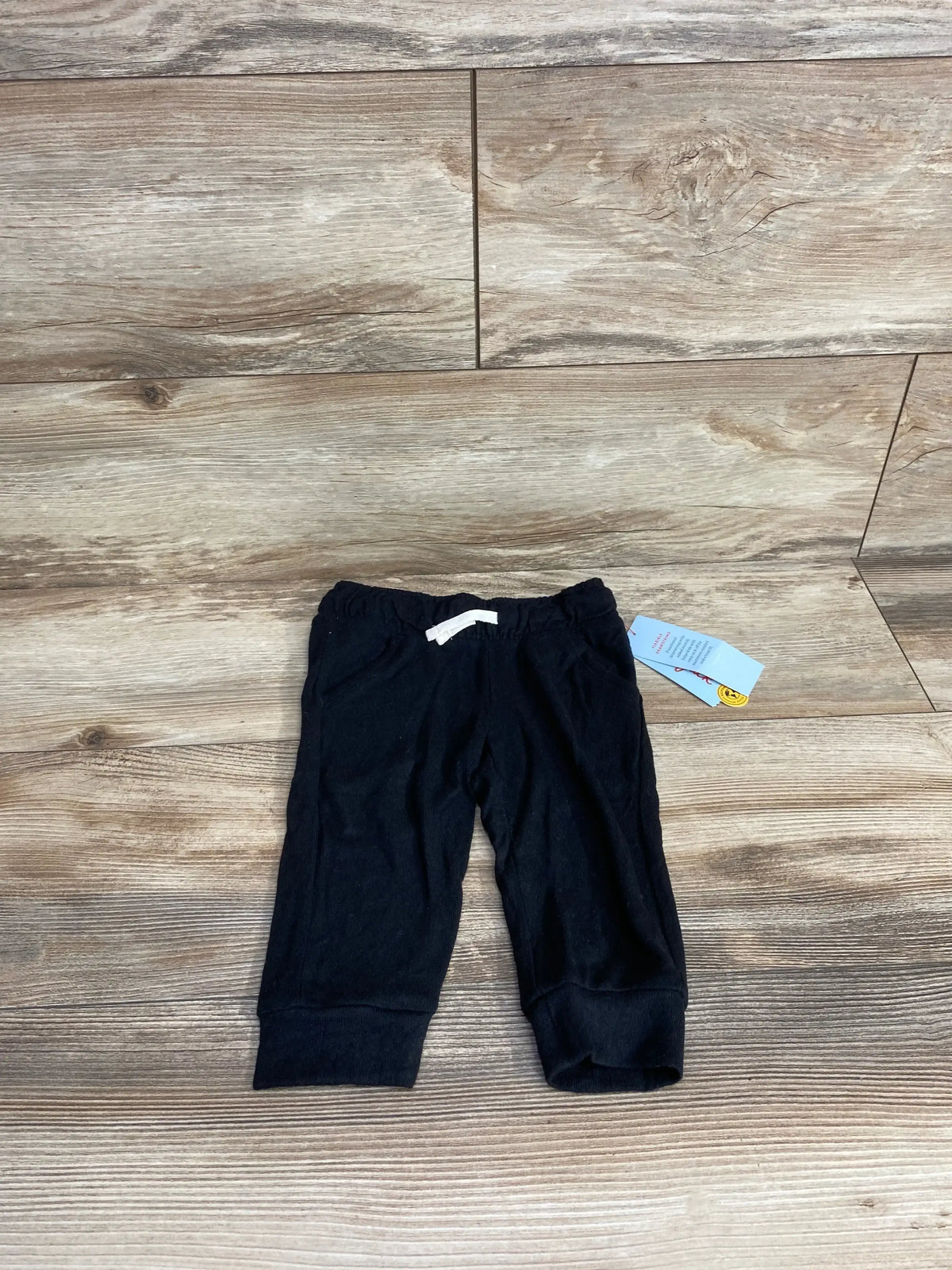 Black baby pants with white drawstring and tag, displayed on wood floor