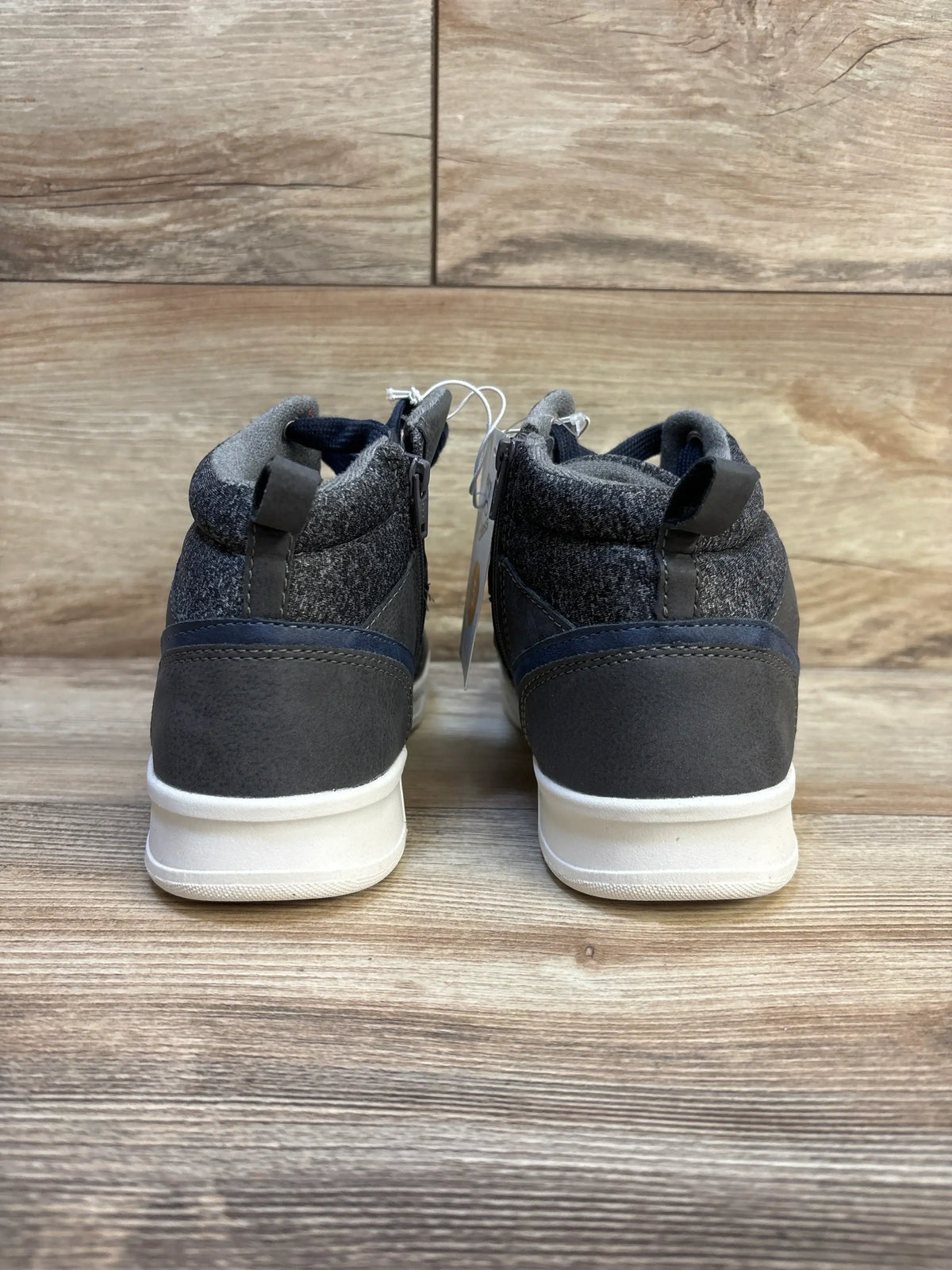 Rear view of gray and navy kids high top sneakers with white soles on wood floor