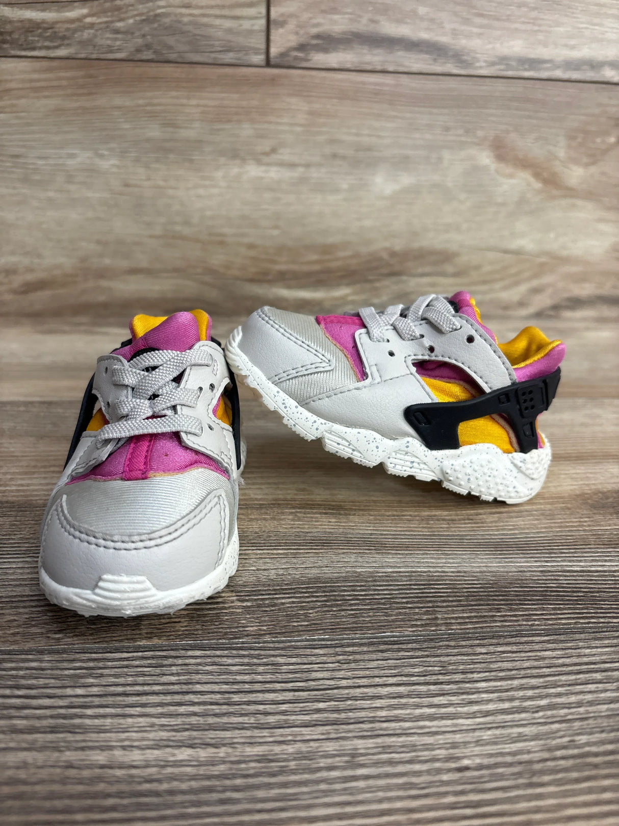 Gray, pink, and yellow toddler sneakers with velcro straps on wood floor