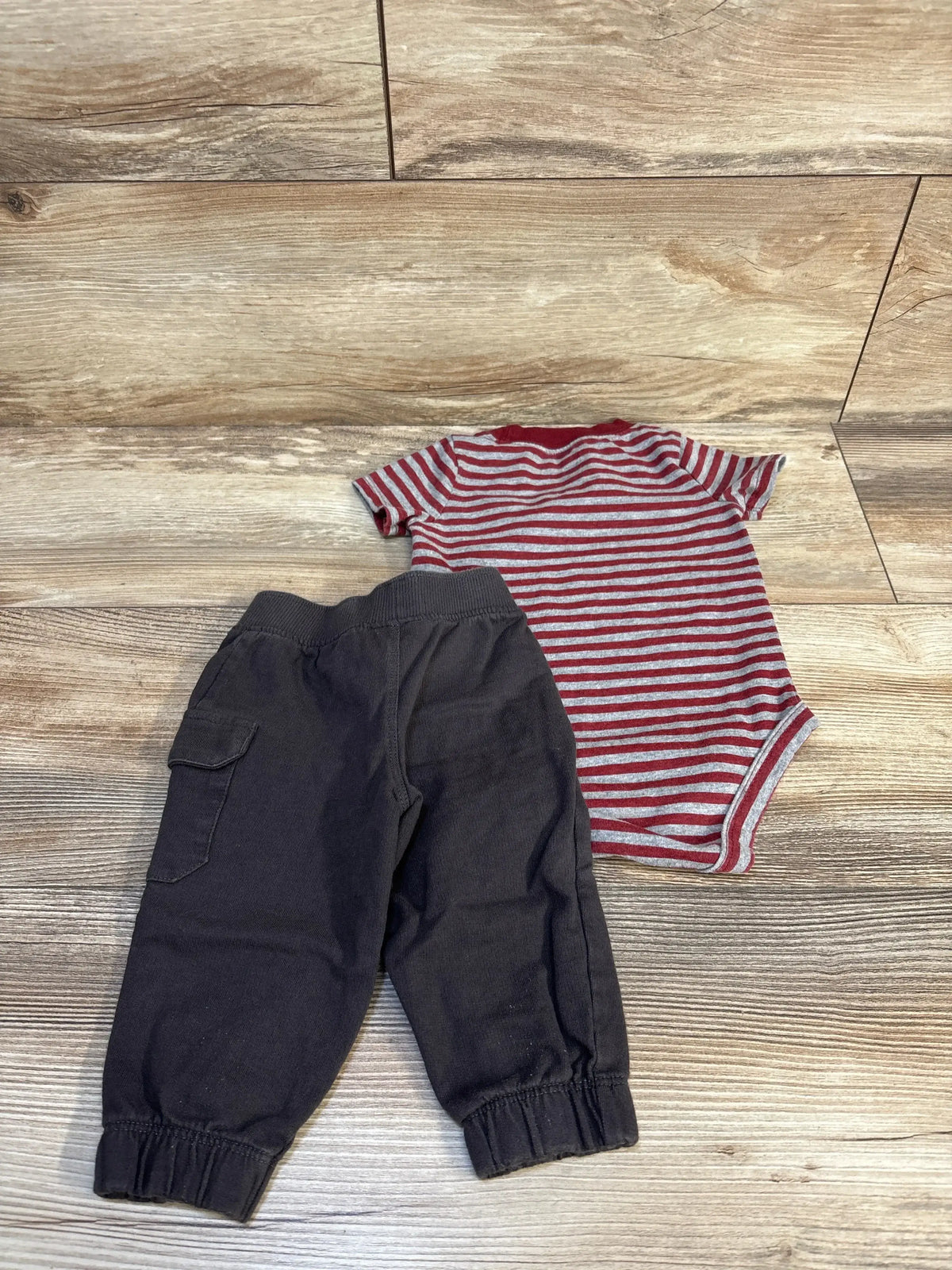 Infant red striped bodysuit and black cargo pants on wood floor, baby clothing set
