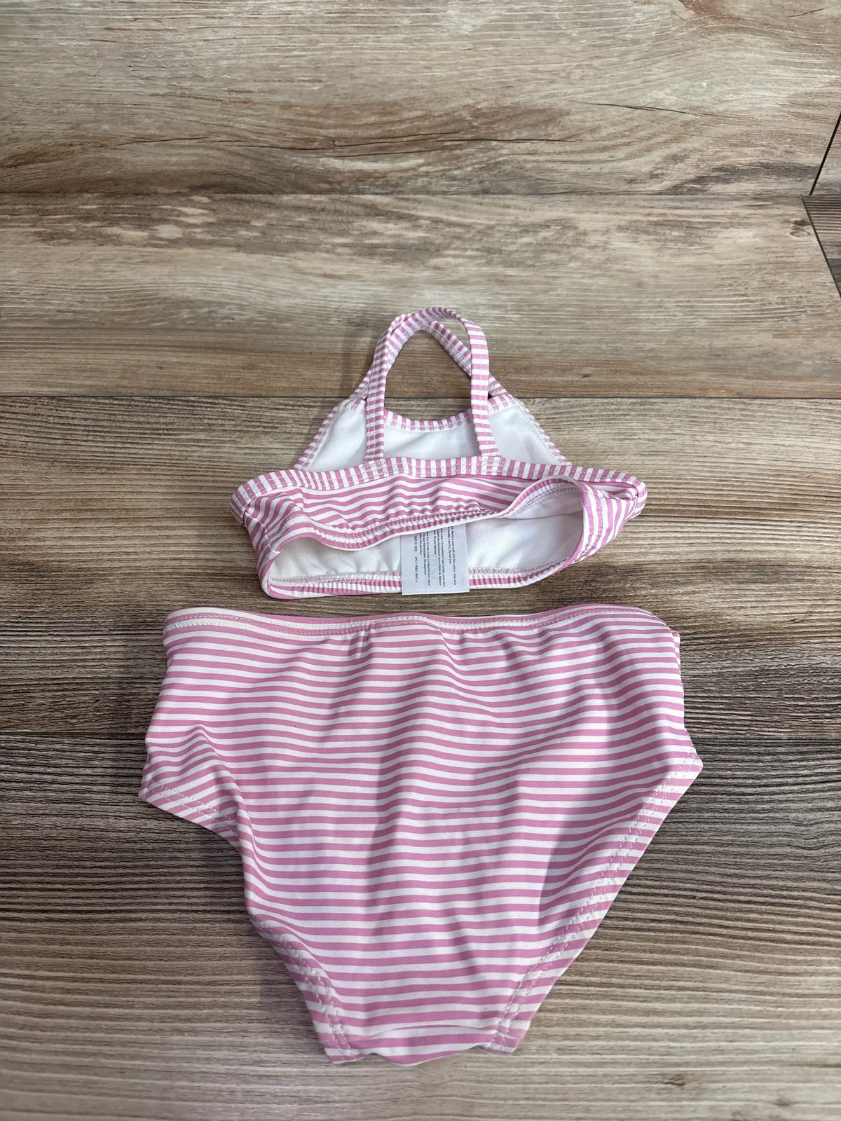 Top-down view of Carter's two-piece pink and white striped baby swimsuit showing halter-style top and high-waist bottoms on wood background