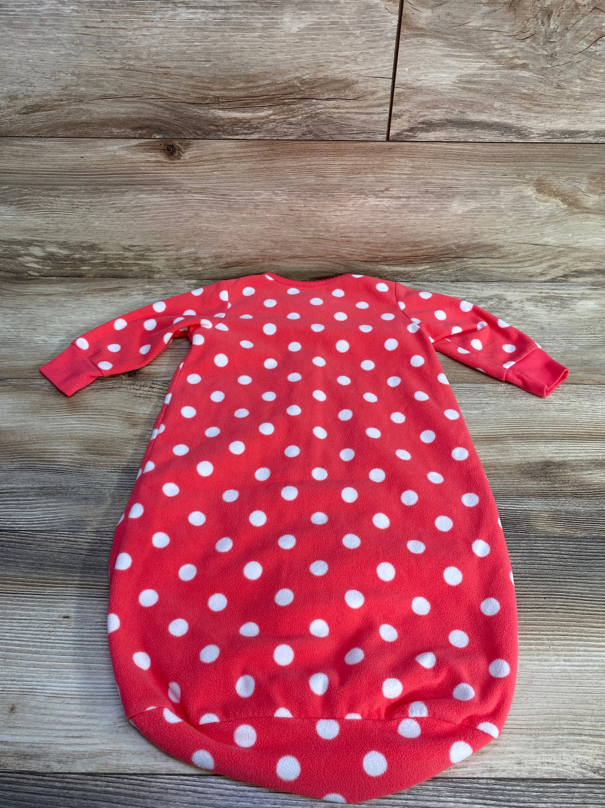 Red baby sleep sack with white polka dots laid flat on wooden floor
