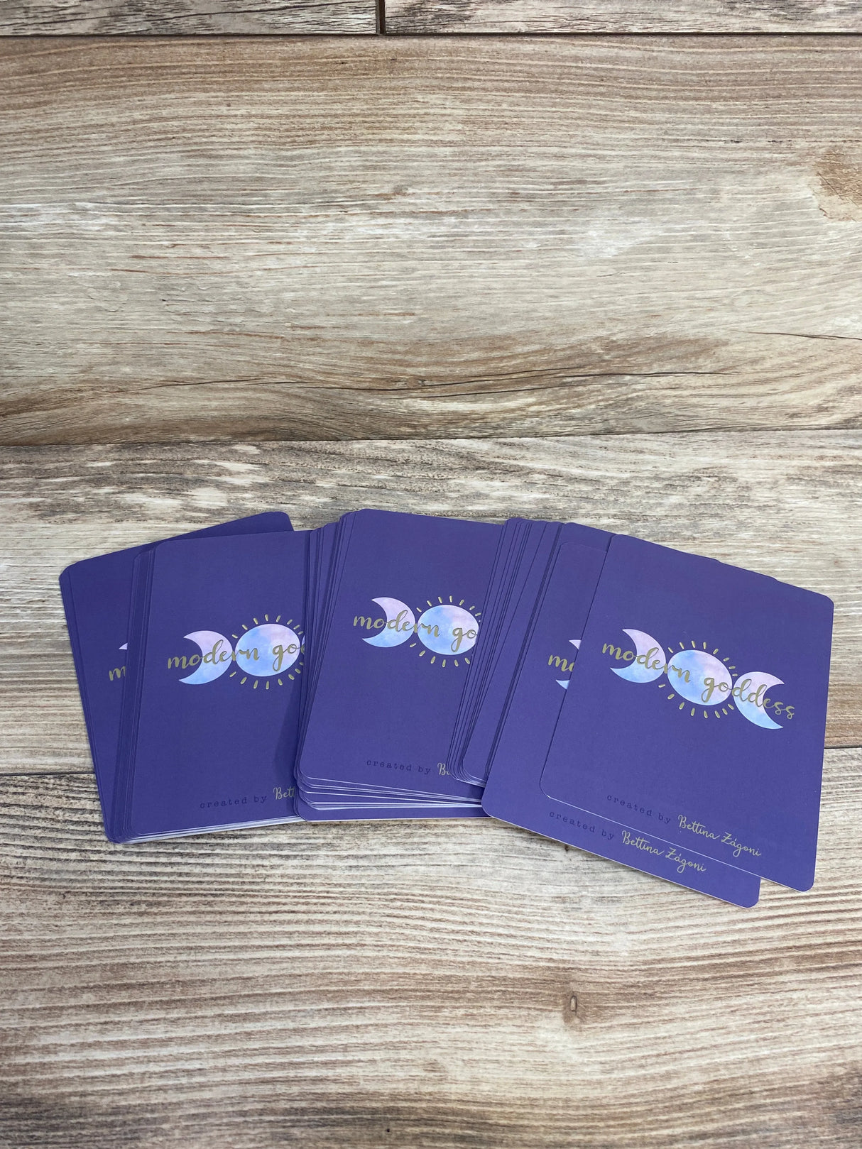 Top-down view of Pregnancy and Birth 52 affirmation cards showcasing purple backs with modern goddess moon logo fanned on a light wood surface