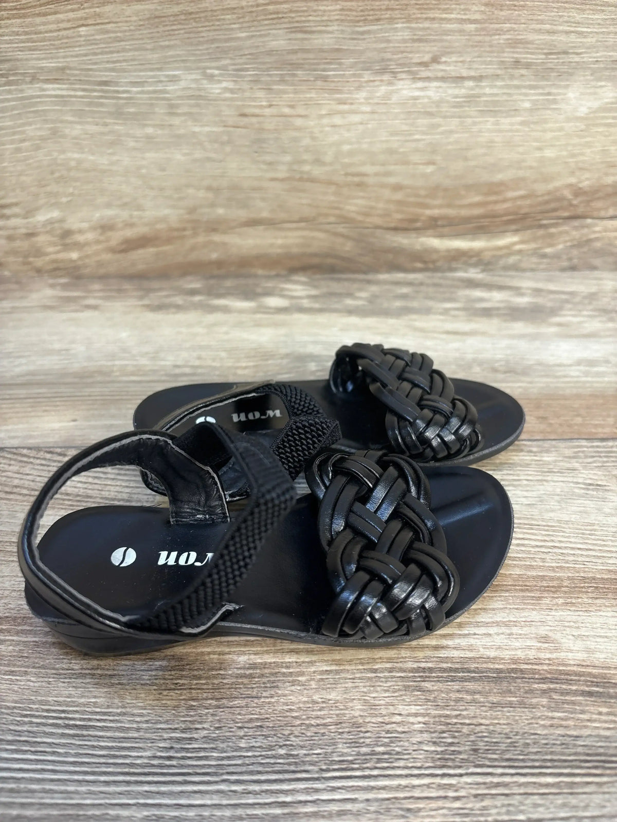 Black woven toddler sandals with ankle straps on wood background
