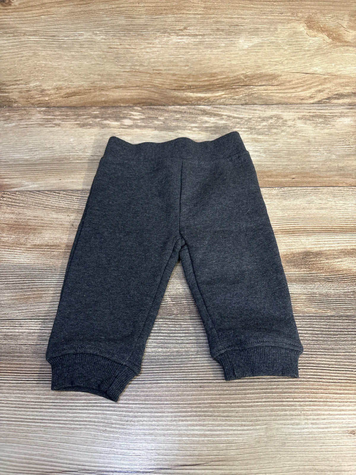 Front view of grey baby joggers showcasing elastic waistband and cuffed ankles on a wood-grain background