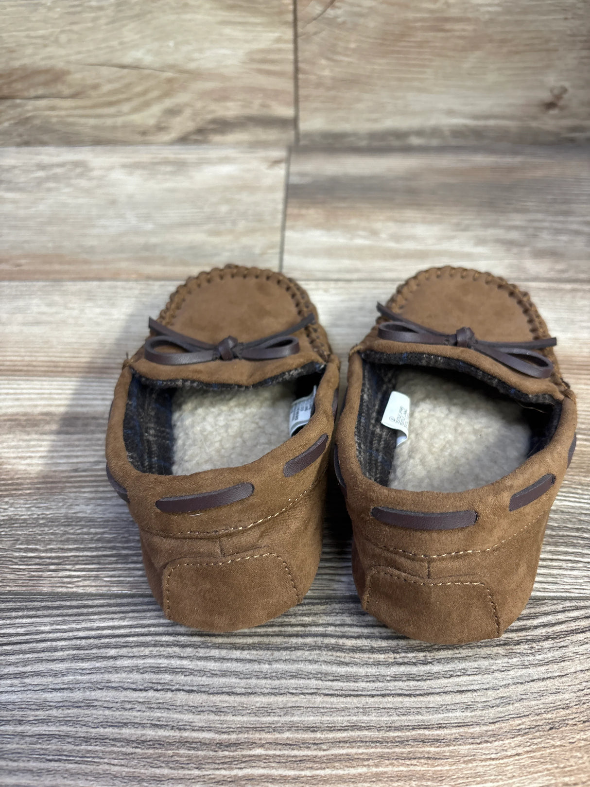 Top rear view of Cat & Jack Lionel toddler moccasin slippers showing brown suede upper, faux-shearling lining, stitched detail and bow on wood background
