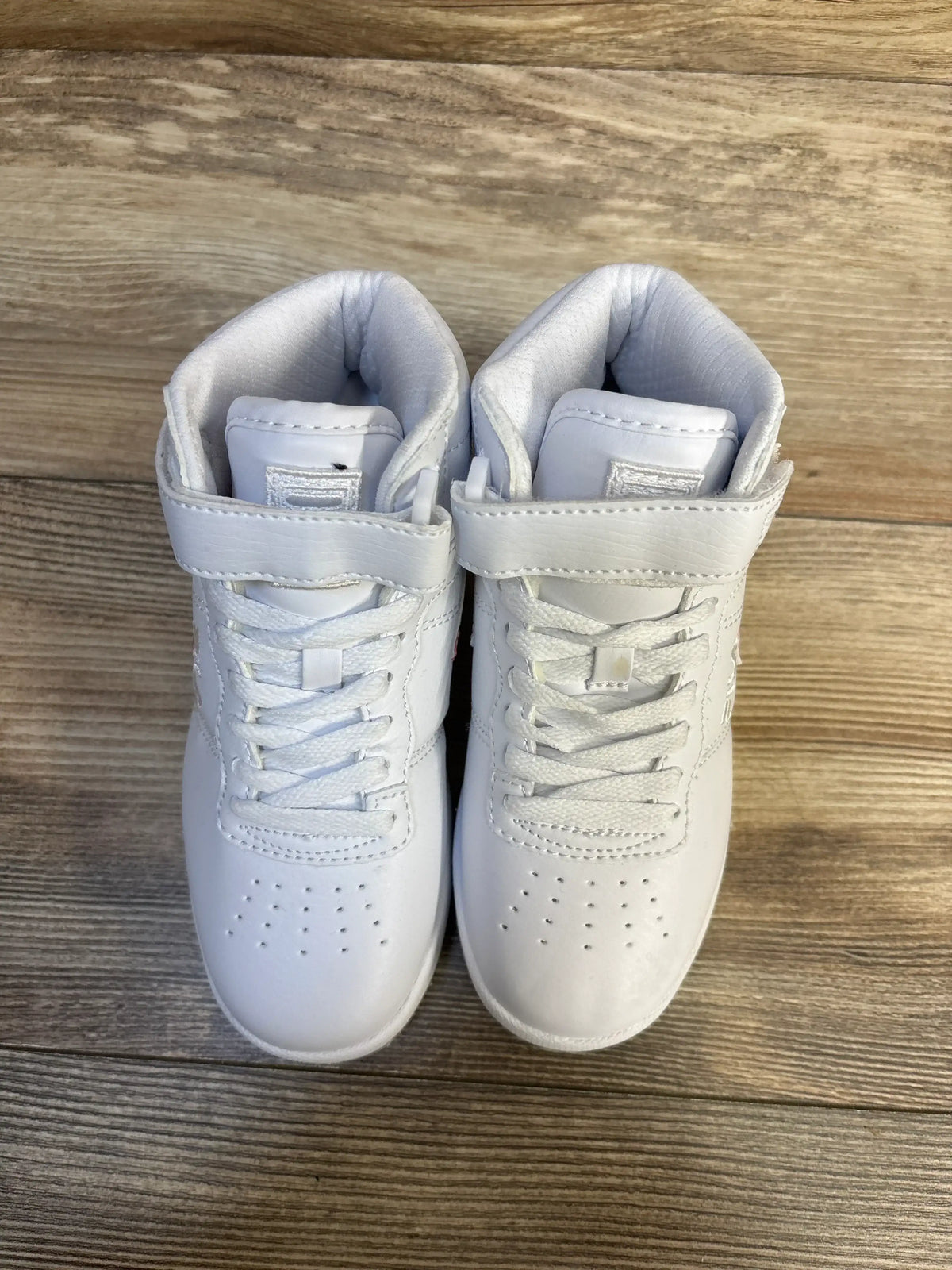 White toddler sneakers with laces and velcro straps on wood floor