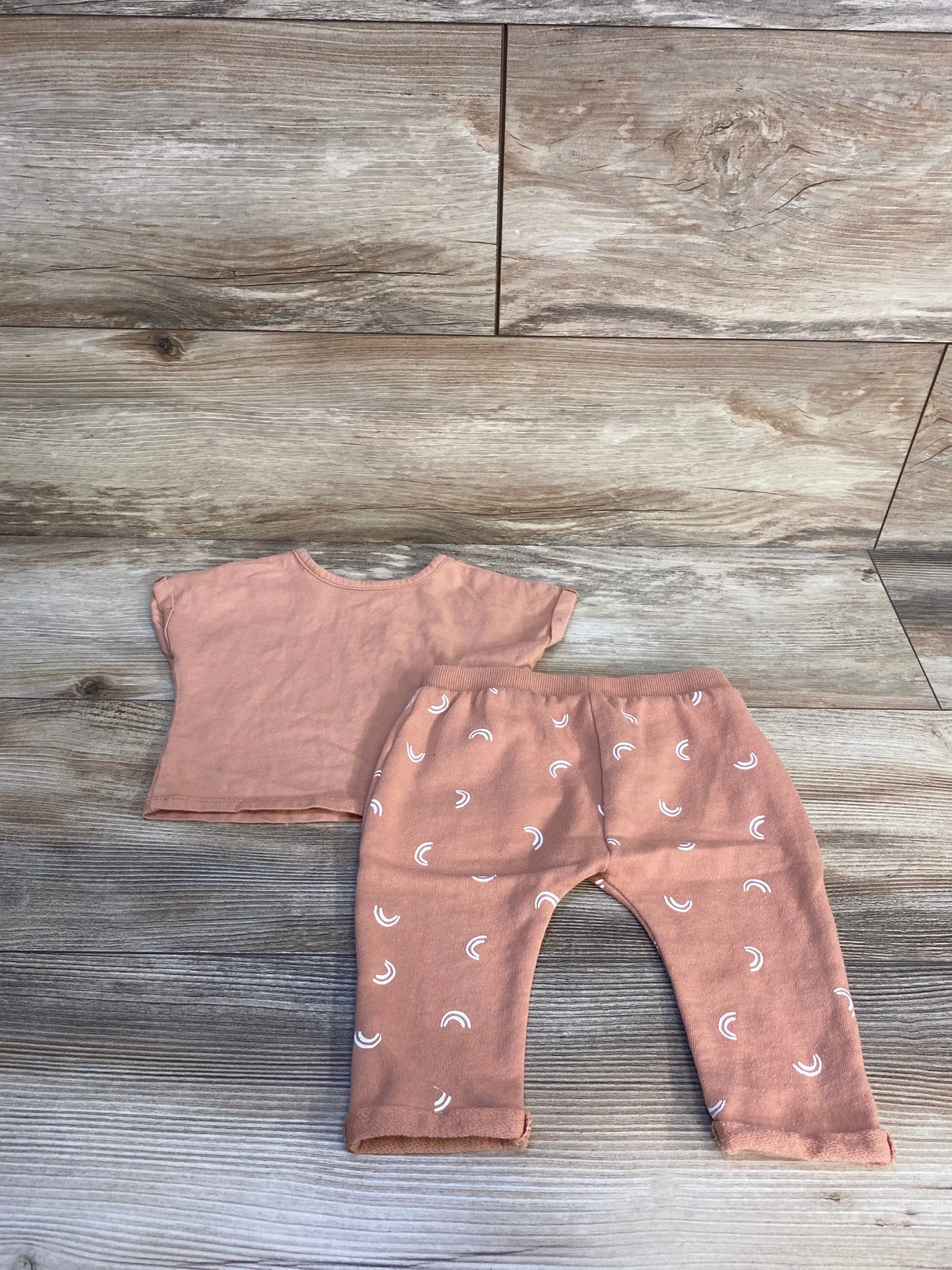 Peach baby outfit set with short sleeve top and rainbow print pants on wood background