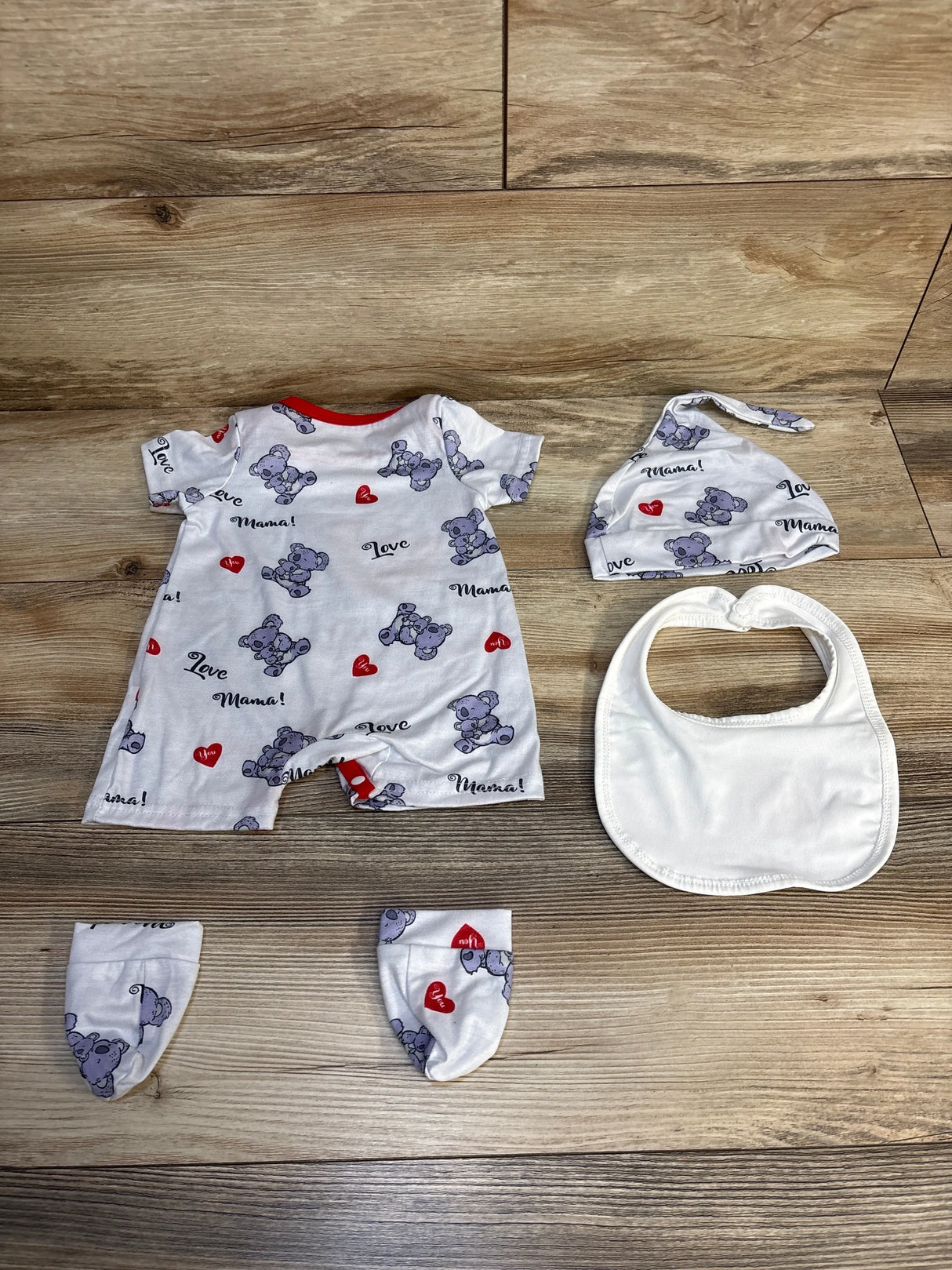 Baby outfit set with koala print, hat, mittens, and bib on wood background