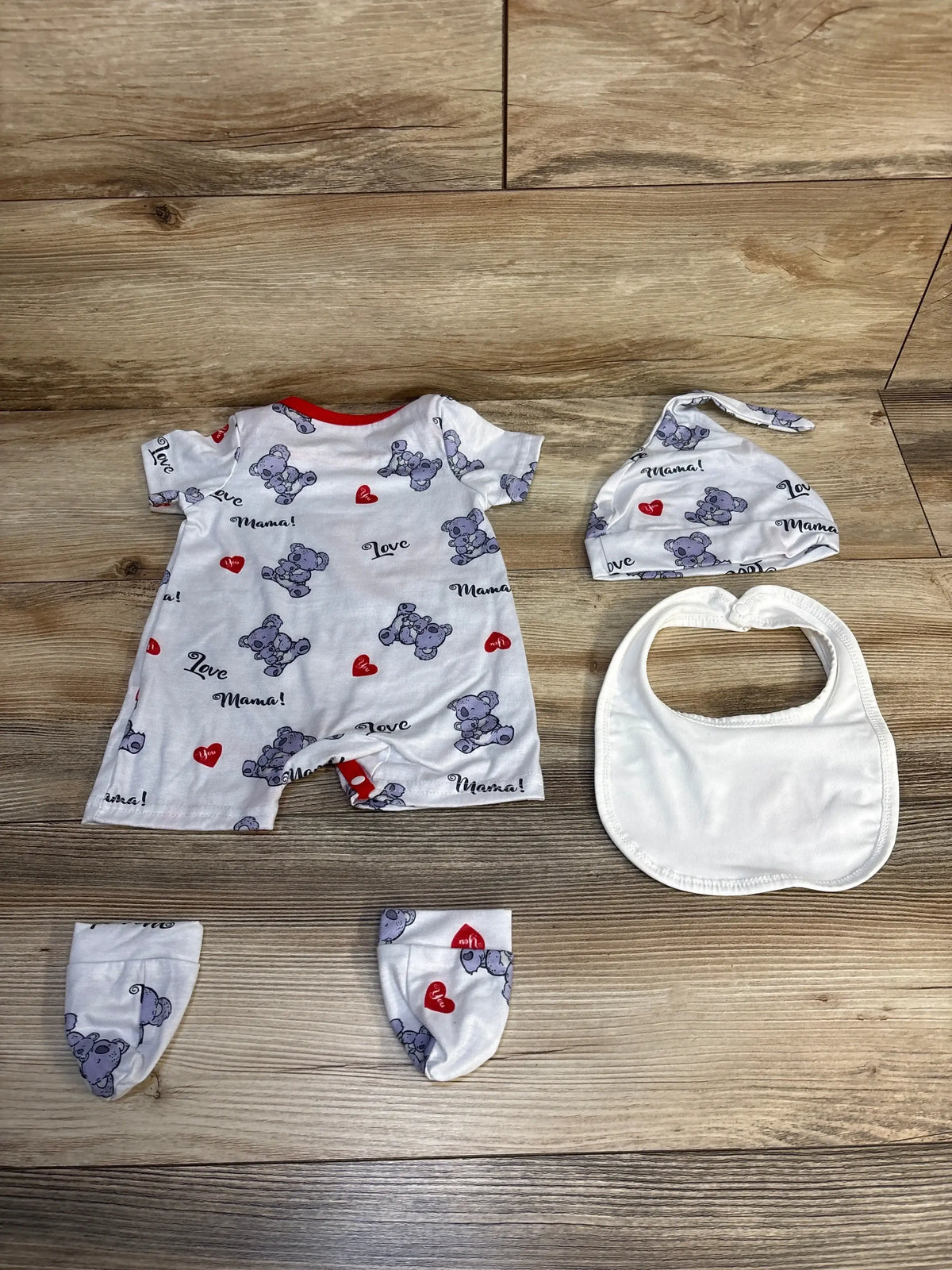 Baby outfit set with koala print, hat, mittens, and bib on wood background