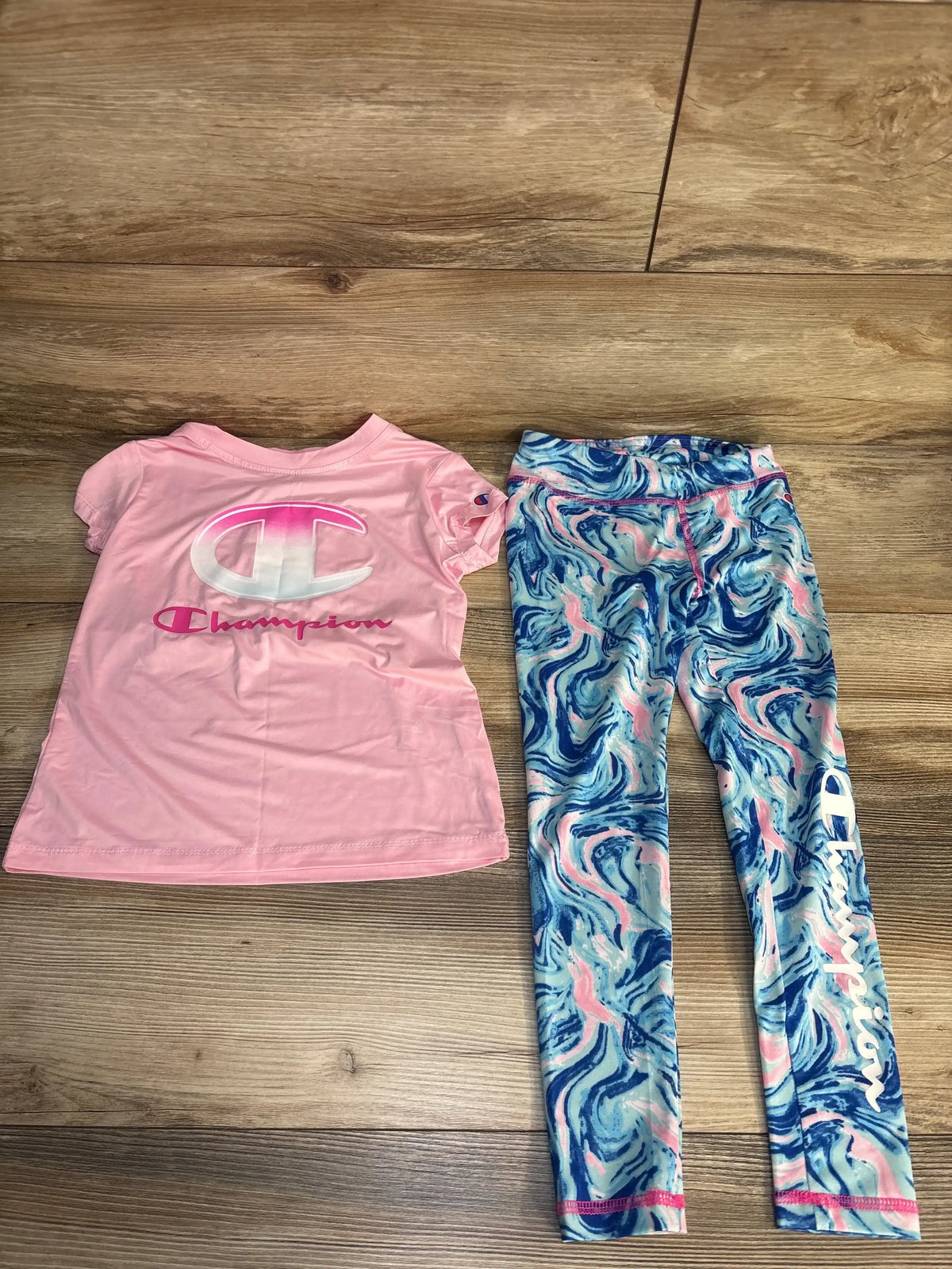 Pink Champion kids t-shirt with logo and blue pink swirl leggings set on wood floor