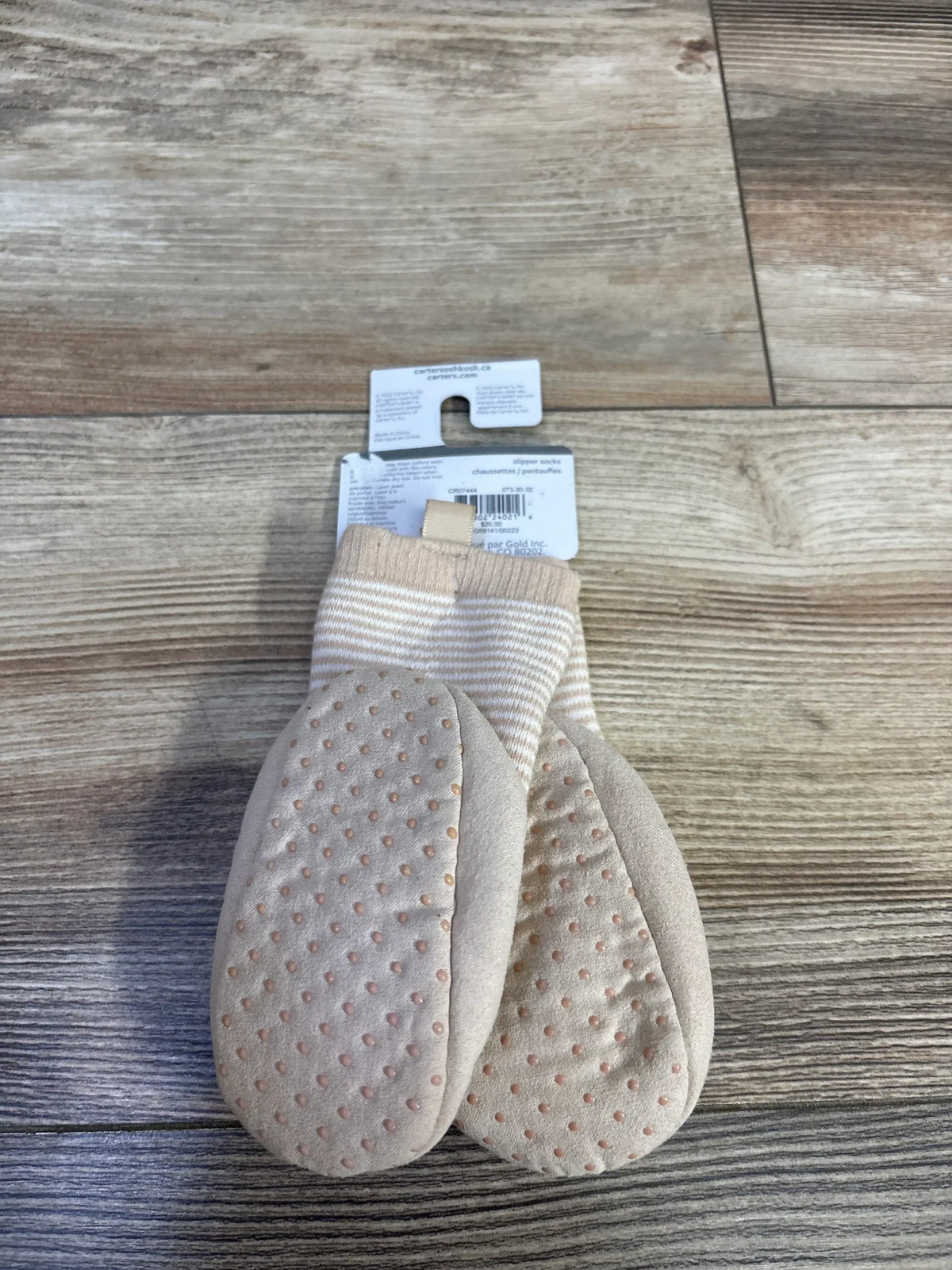 Top-down view of Carter's baby goose rattle slippers showing beige striped cuff and non-slip dotted soles on wood floor
