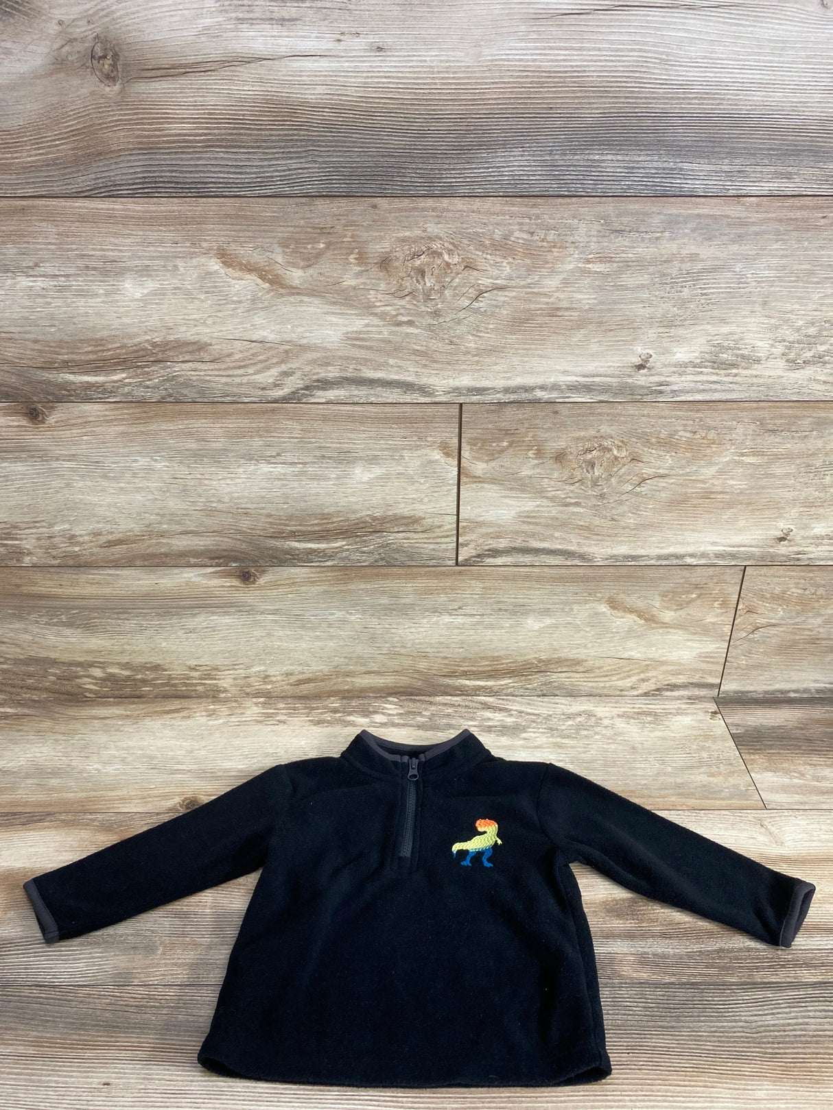 Front view of black Cat and Jack fleece jacket size 18m with quarter zip closure and dinosaur embroidery on wood background