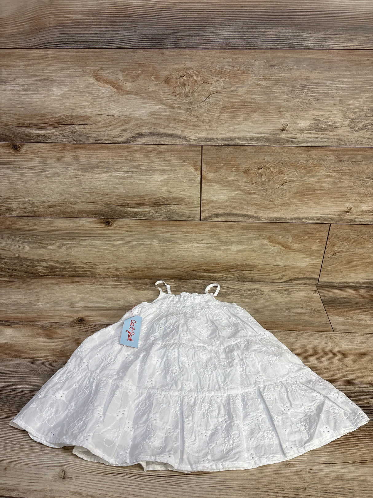 Flat lay of Cat & Jack white toddler eyelet dress showing smocked top, thin straps and tiered skirt on wood floor