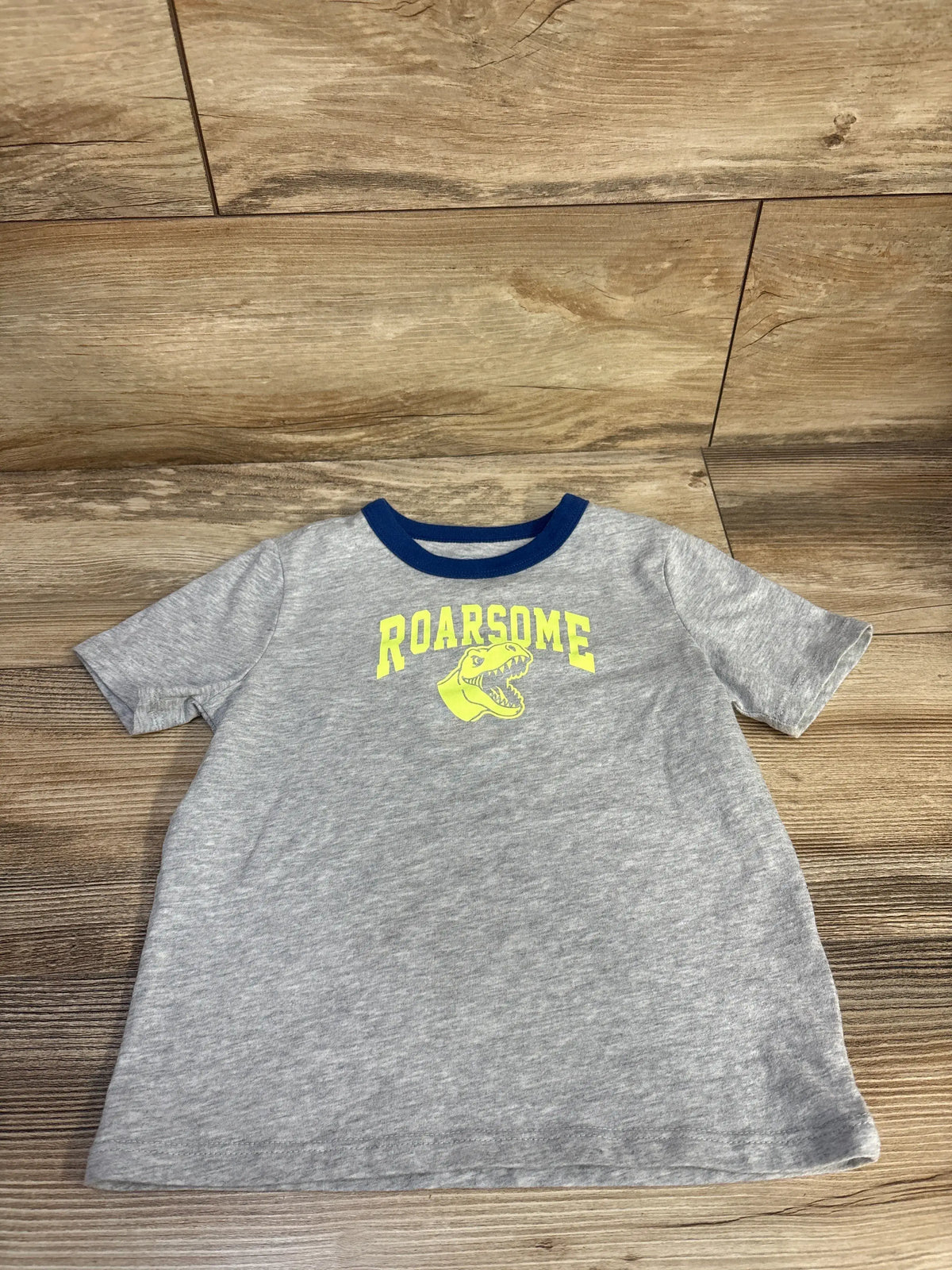 Front view of Wonder Nation Roarsome shirt in grey showcasing a yellow dinosaur graphic and blue crew neck trim on wood flooring