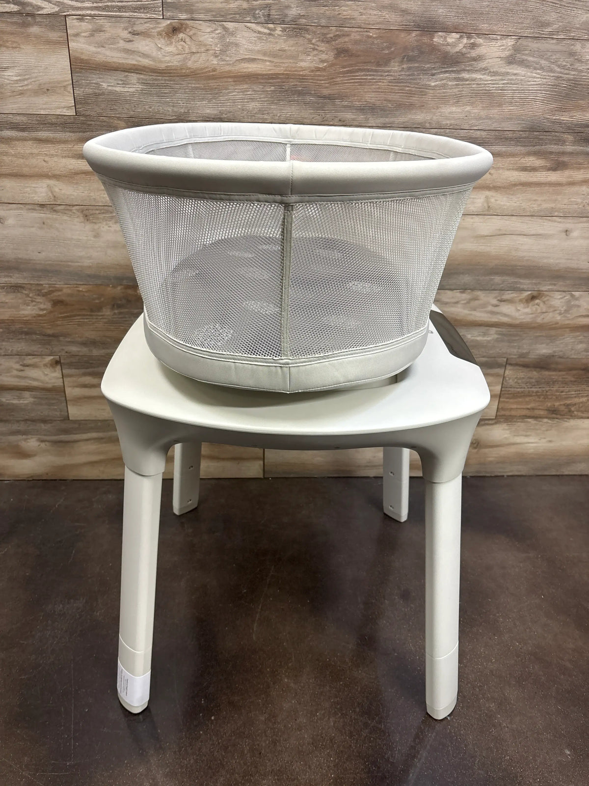 Front view of 4moms mamaRoo Sleep Bassinet showcasing a white mesh-sided bassinet on a stand with wood-paneled background