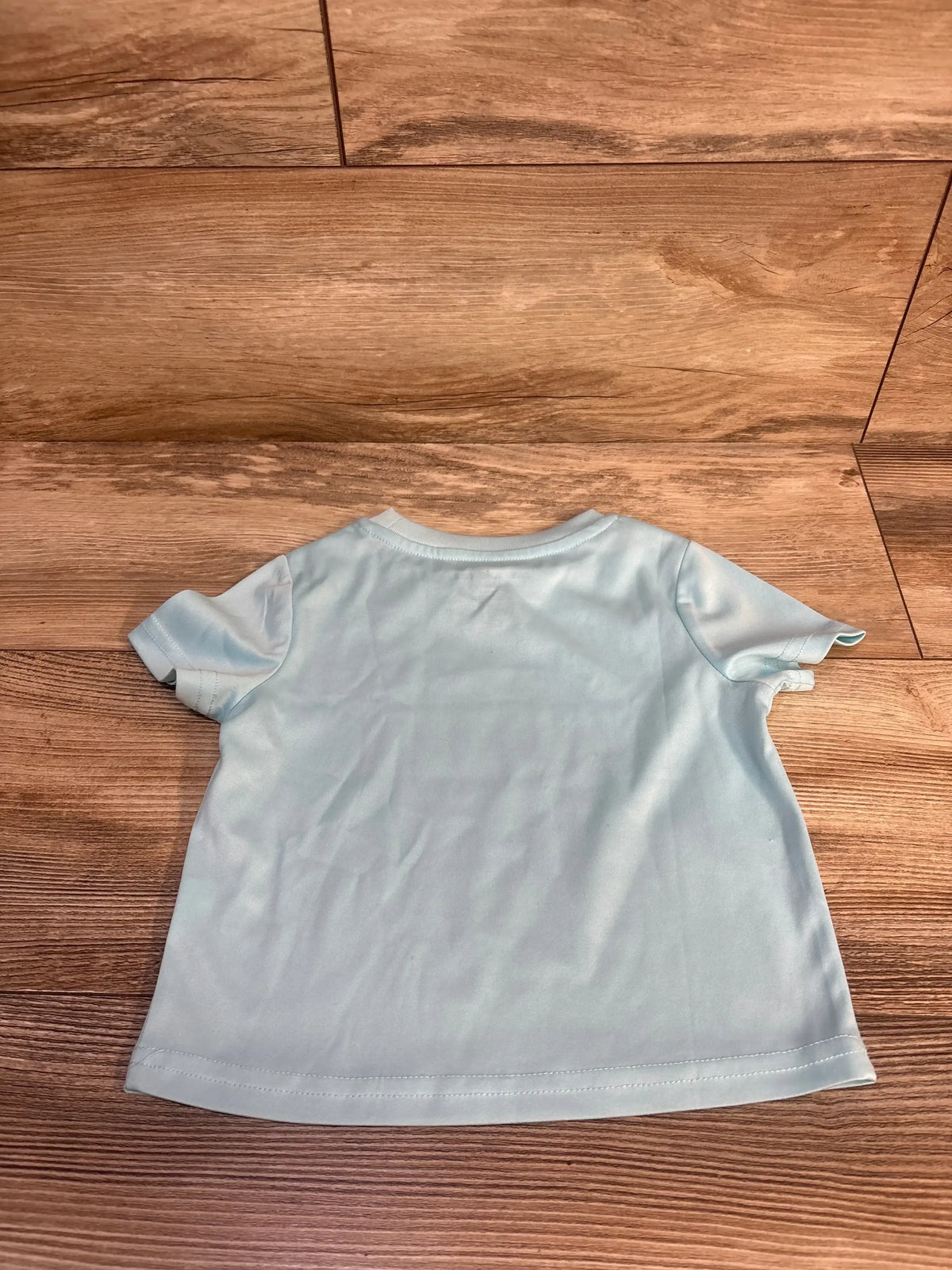 Light blue toddler t-shirt laid flat on wood floor, kids clothing resale