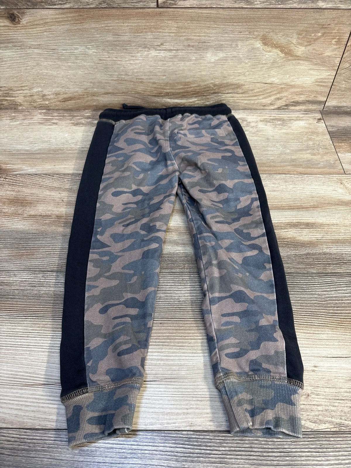 Kids camo jogger pants with black side panels on rustic wood background