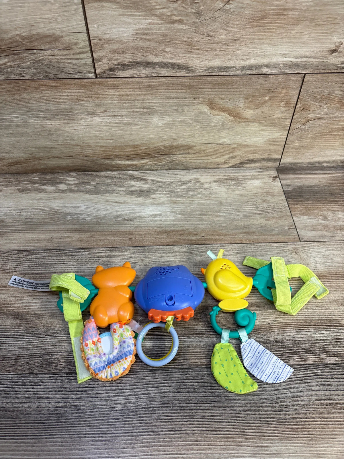 Overhead view of Infantino Go gaga Musical Travel Bar Activity Toy showcasing colorful animal attachments, sensory fabrics, rings, and stroller straps on a wood floor