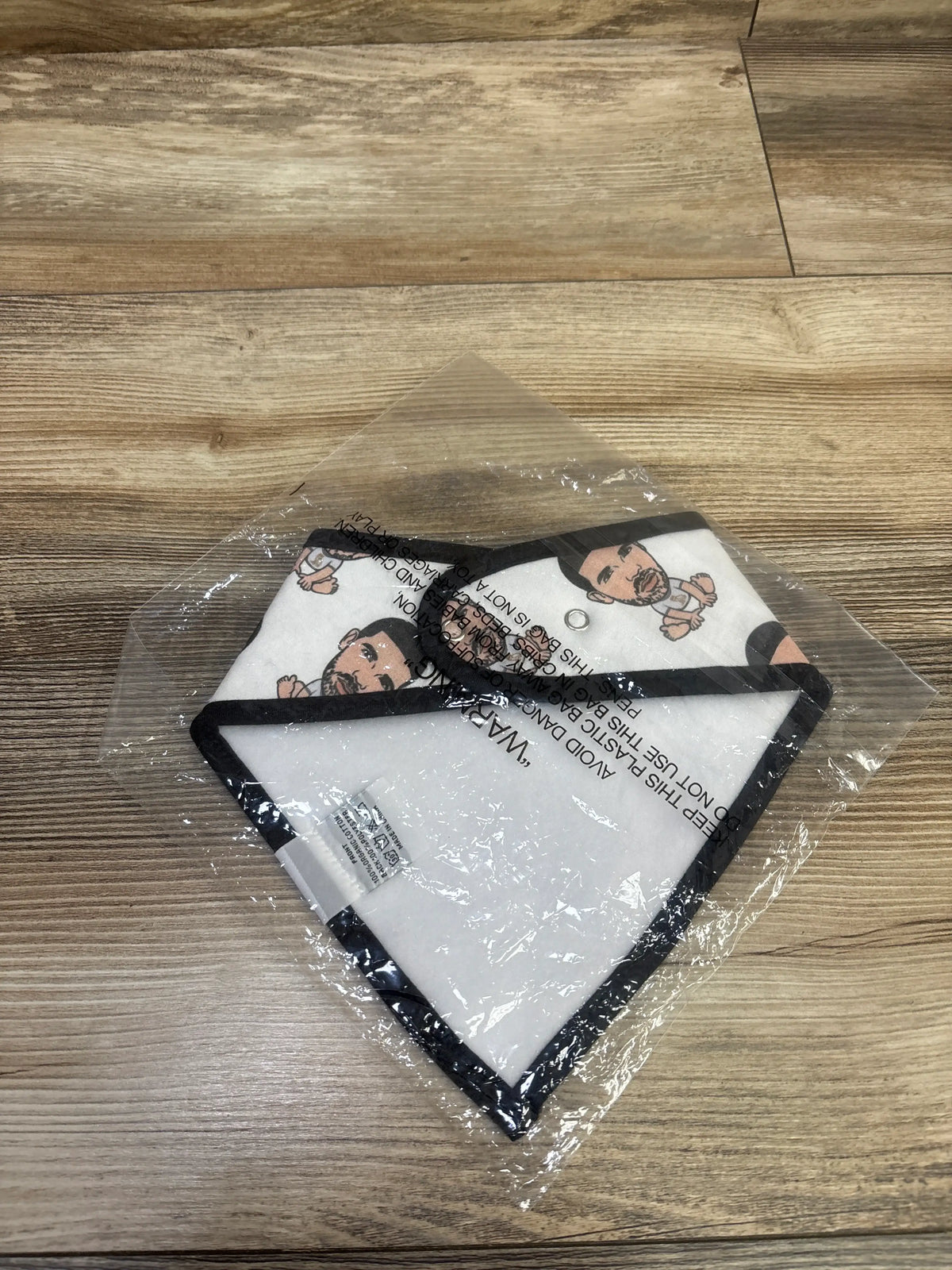 Top view of white Mommy and Cai Company Drake bandana bib with black trim and printed faces in plastic packaging
