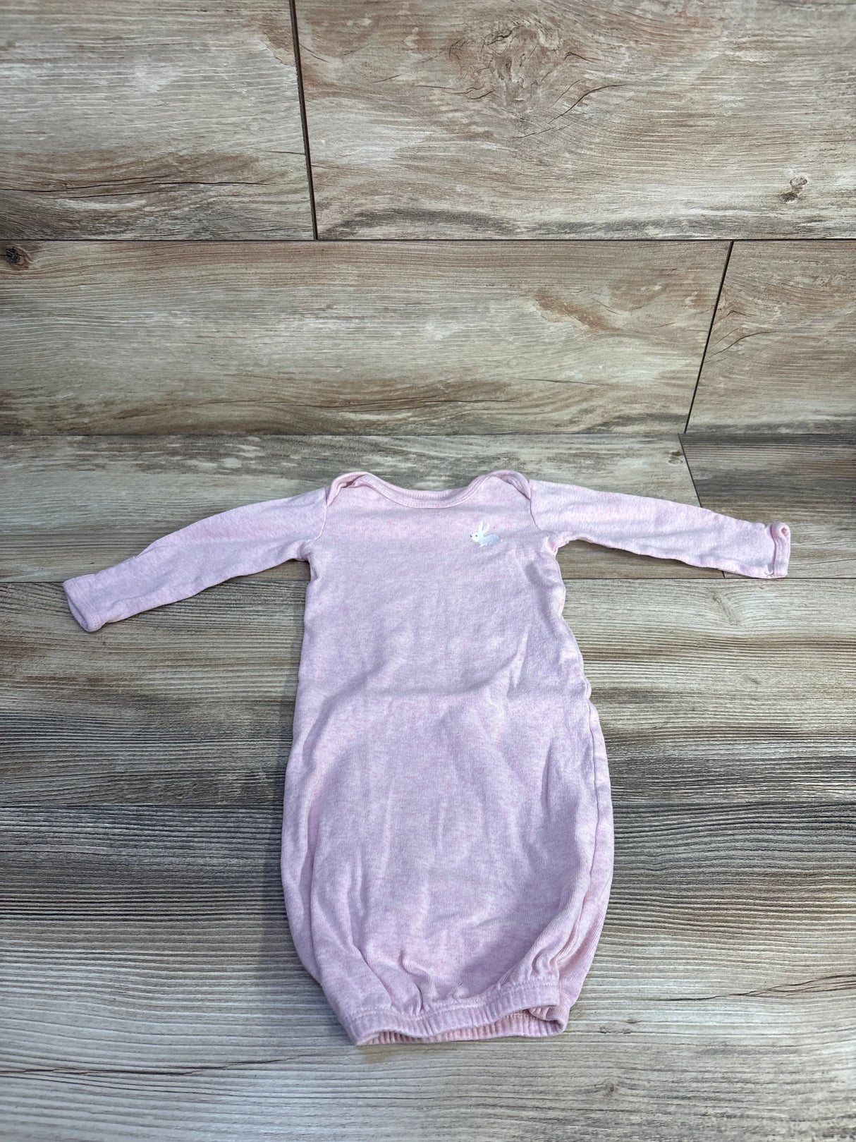 Flat lay of newborn pink Simple Joys sleep gown showing long sleeves, elastic gathered bottom, and small white embroidered bunny on wood background