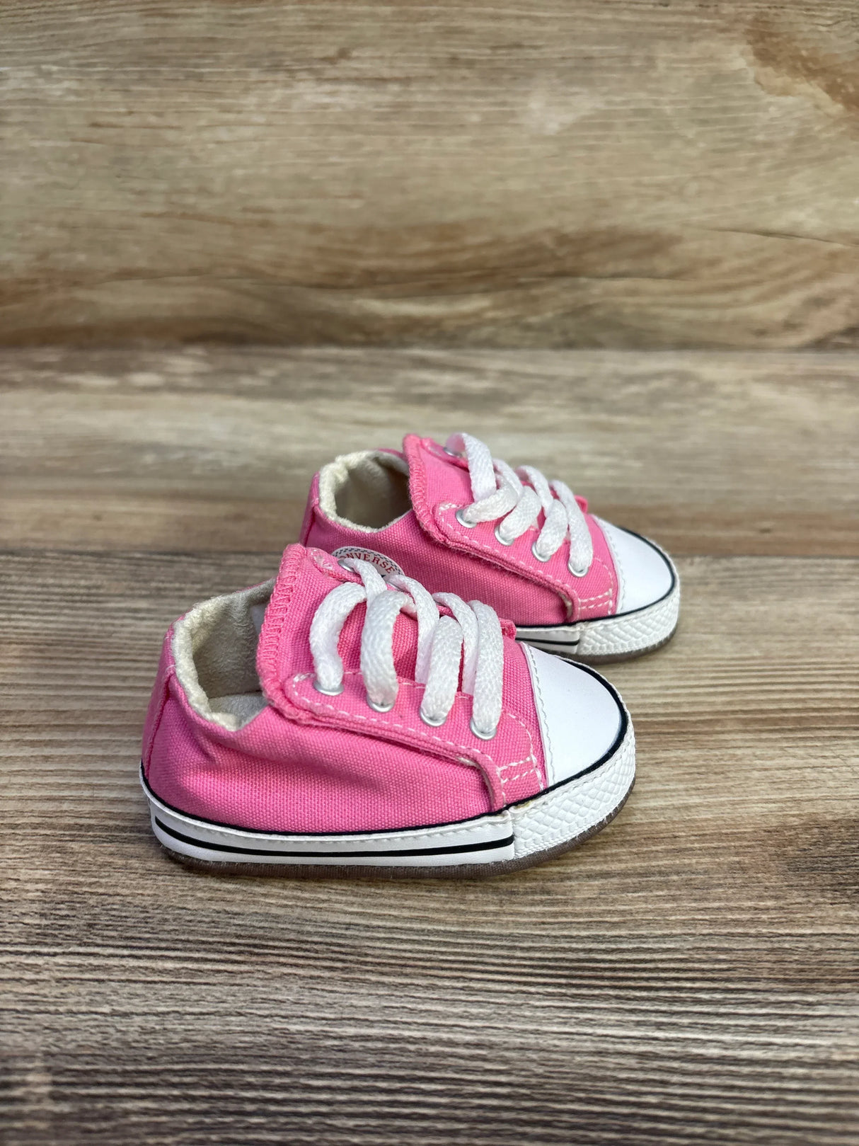 Side view of pink Converse All Star Cribster baby sneakers (size 1C) showing white laces and rubber toe on wood background