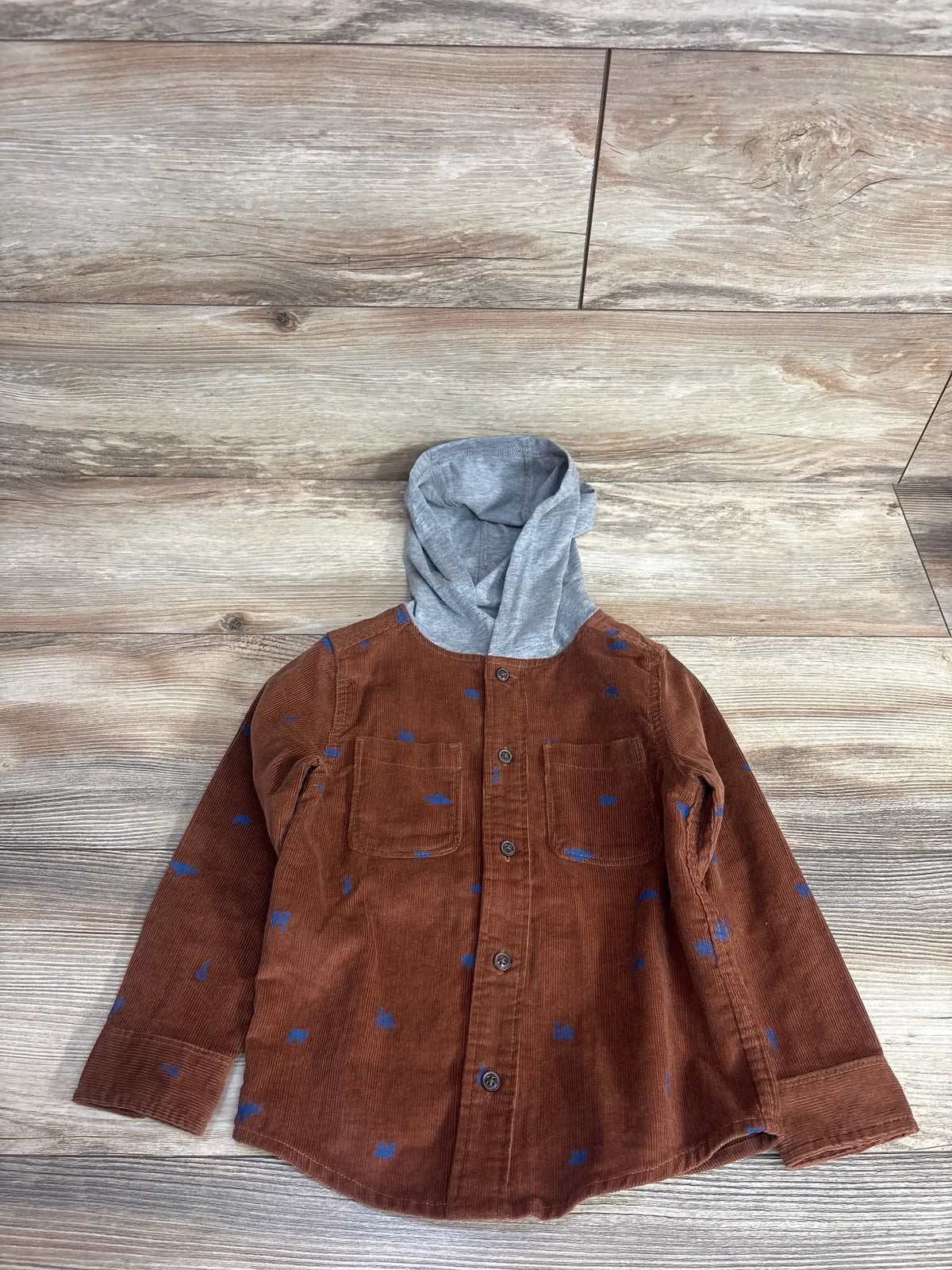 Brown corduroy kids shirt with blue spots, long sleeves, and gray hood on wood floor