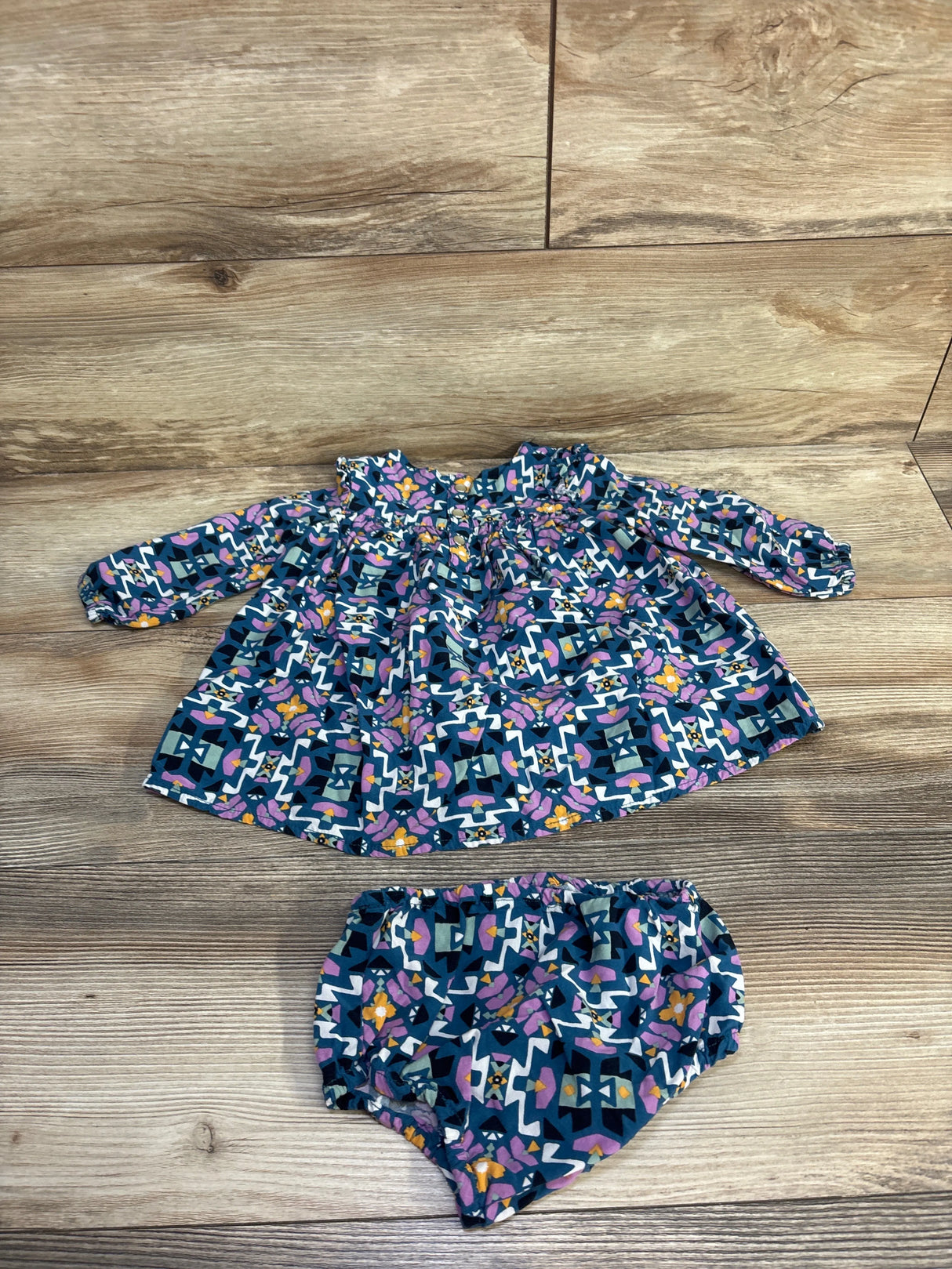 Flat lay of blue Wrangler 2-piece dress and bloomers with smocked long sleeves and geometric floral print on wood