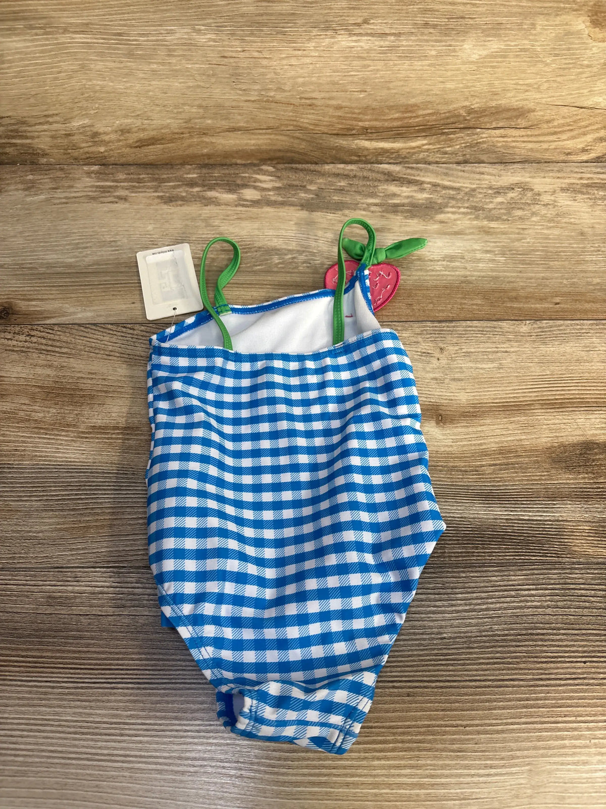 Top view of Adventurewear 360 one-piece swimsuit showcasing a blue-and-white gingham pattern and green straps on wood